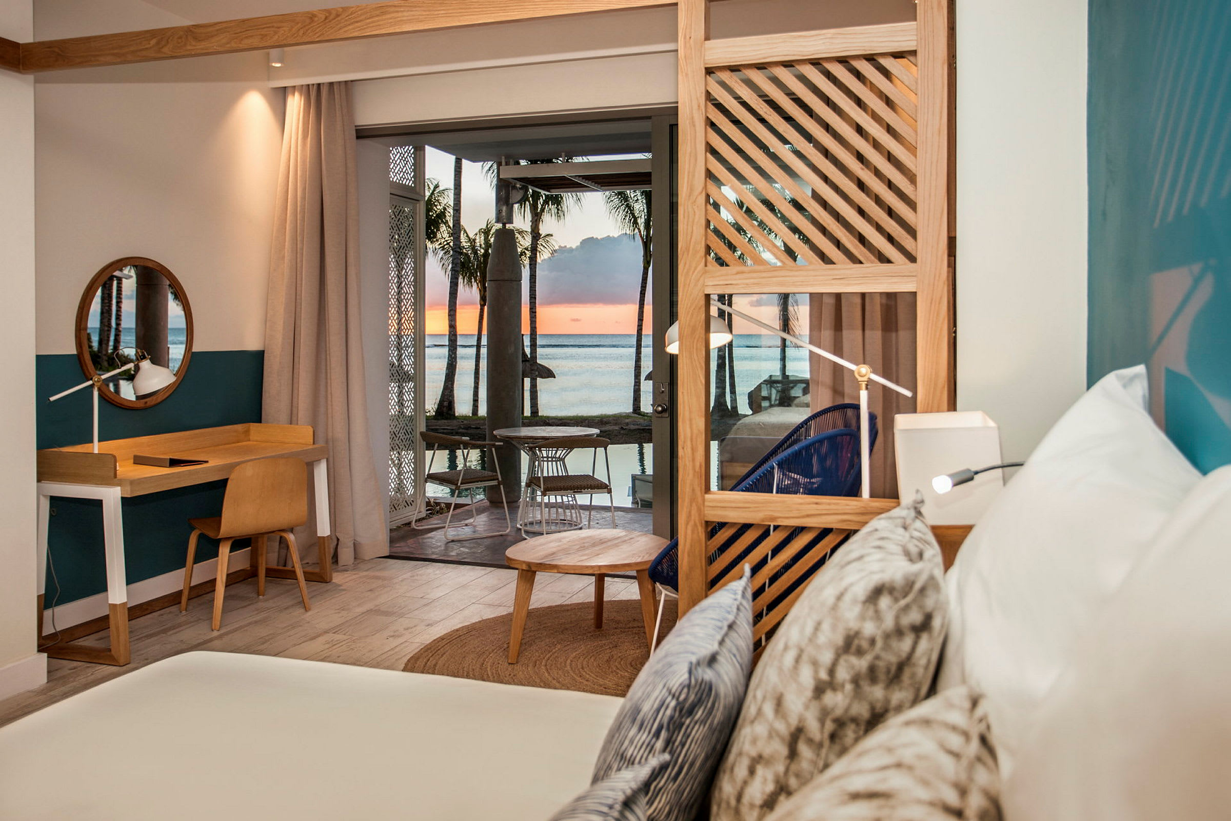 Interiøret i et hotellrom med en seng, skrivebord og utsikt mot havet og solnedgangen. (AI-generert tekst)
