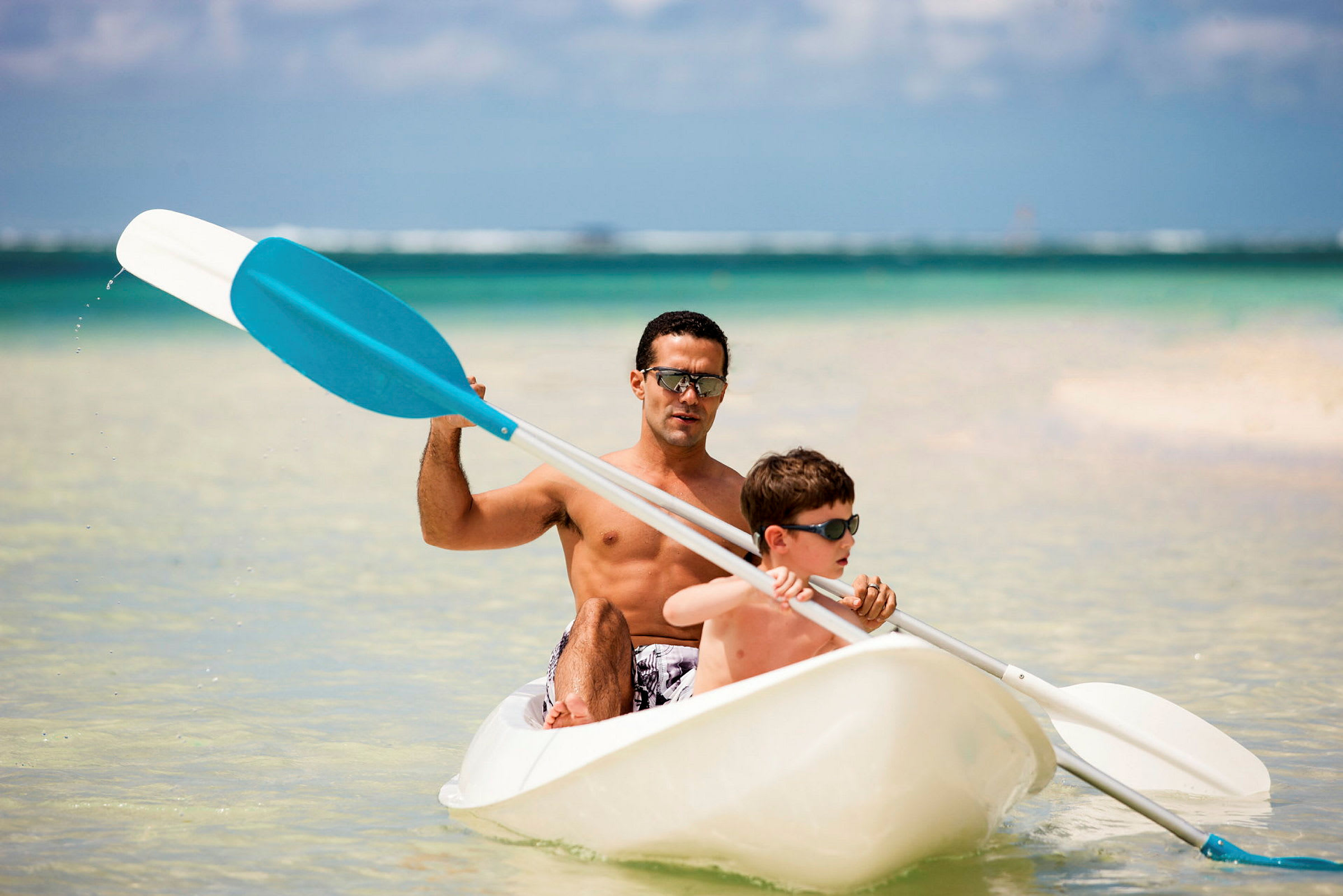To personer padler en kajakk i klart vann ved en strand. (AI-generert tekst)