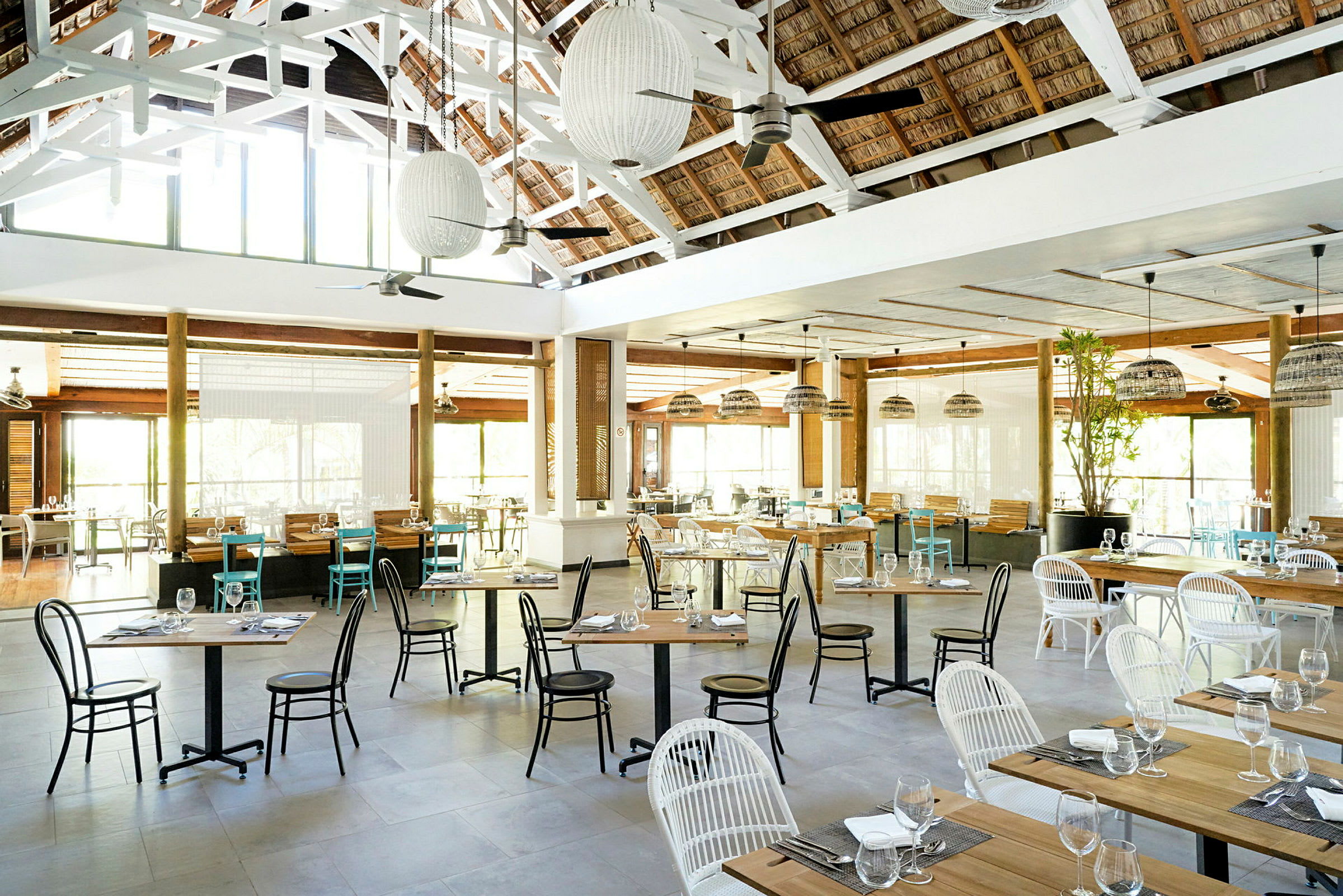 En romslig restaurant med bord og stoler, dekorert med lamper og store vinduer som slipper inn lys. (AI-generert tekst)