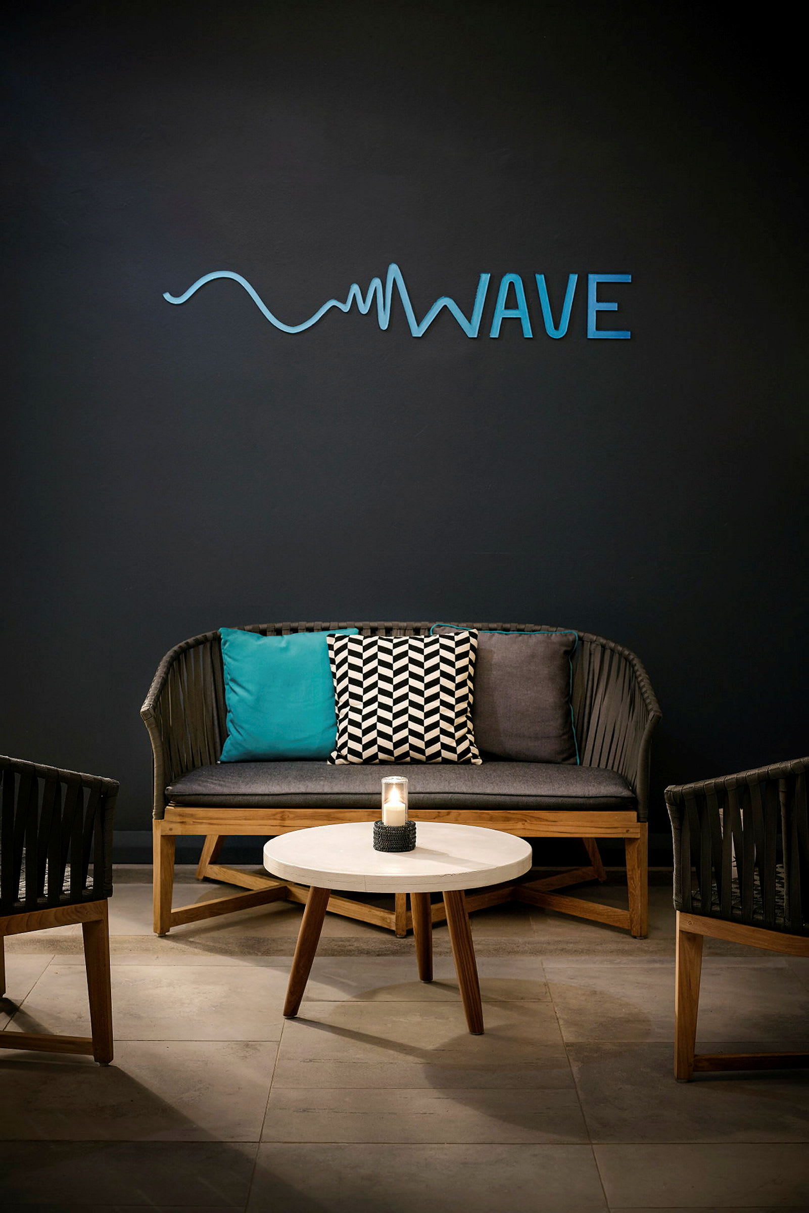 En sittegruppe med en sofa, to stoler, et rundt bord og en vegg med teksten 'Wave'. (AI-generert tekst)