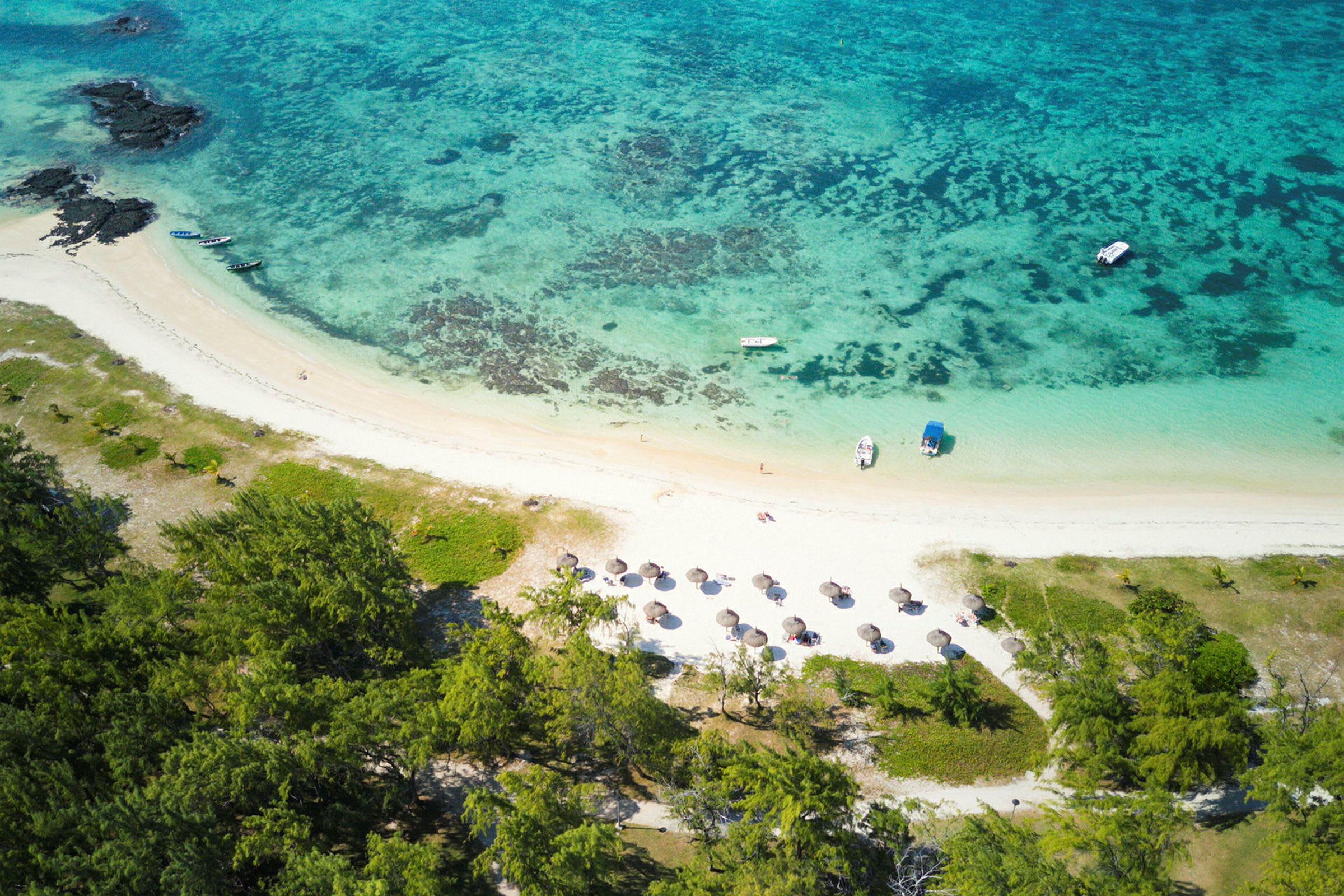 Luftfoto av en tropisk strand med parasoller, båter og omliggende grøntområder. (AI-generert tekst)