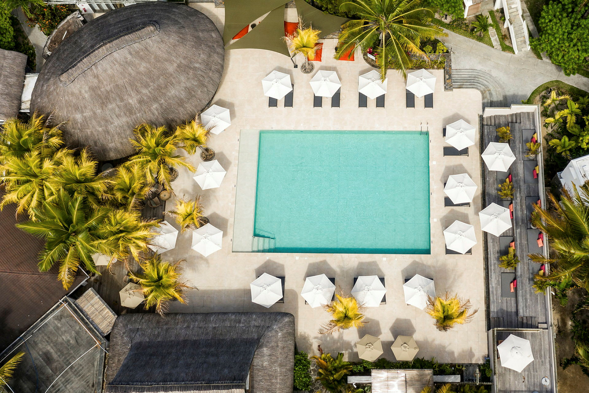Flyfoto av et strandnært hotellbasseng omgitt av parasoller og solsenger. (AI-generert tekst)