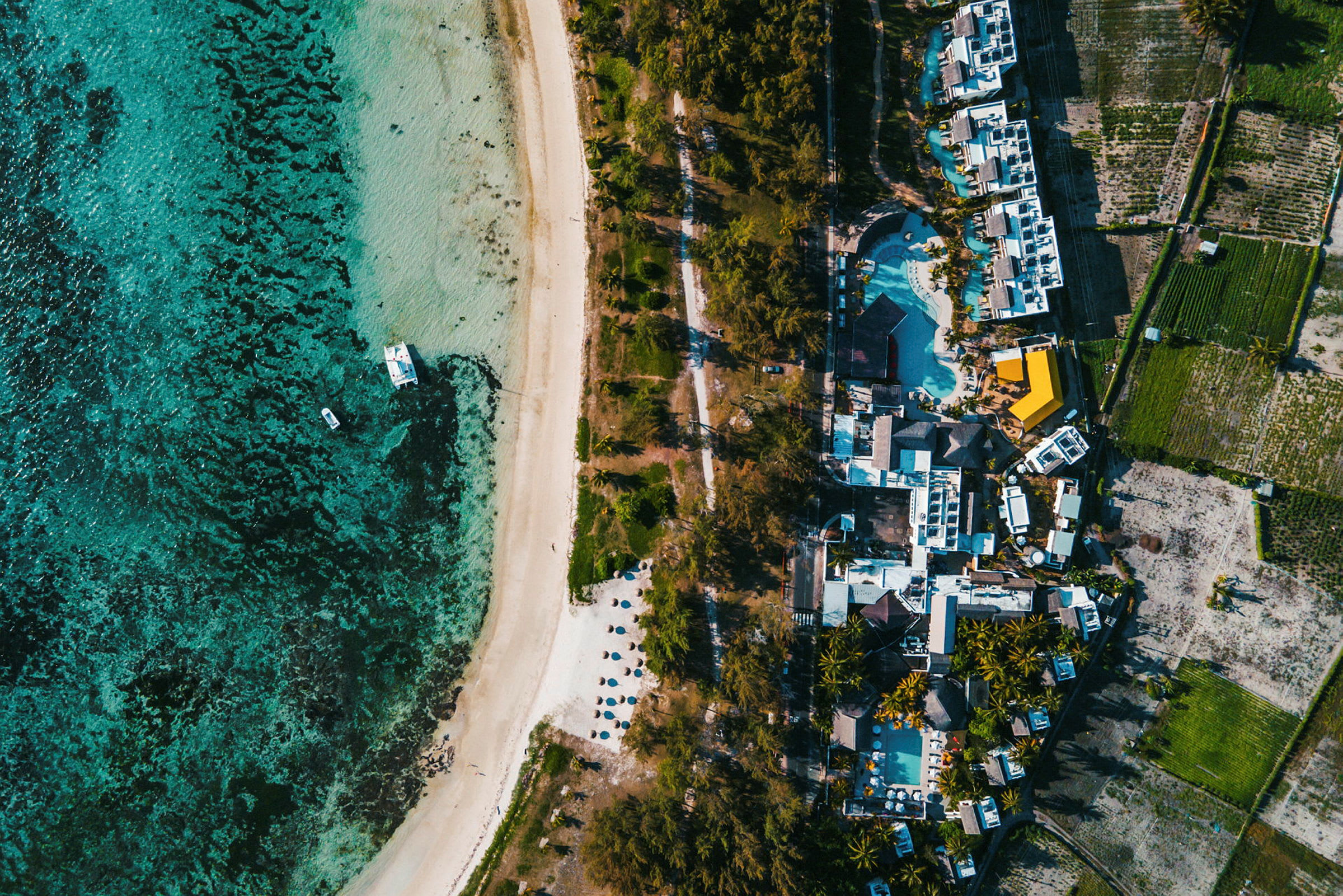 Et flyfoto av en strand ved havet, med bygninger og grøntområder ved siden av. (AI-generert tekst)