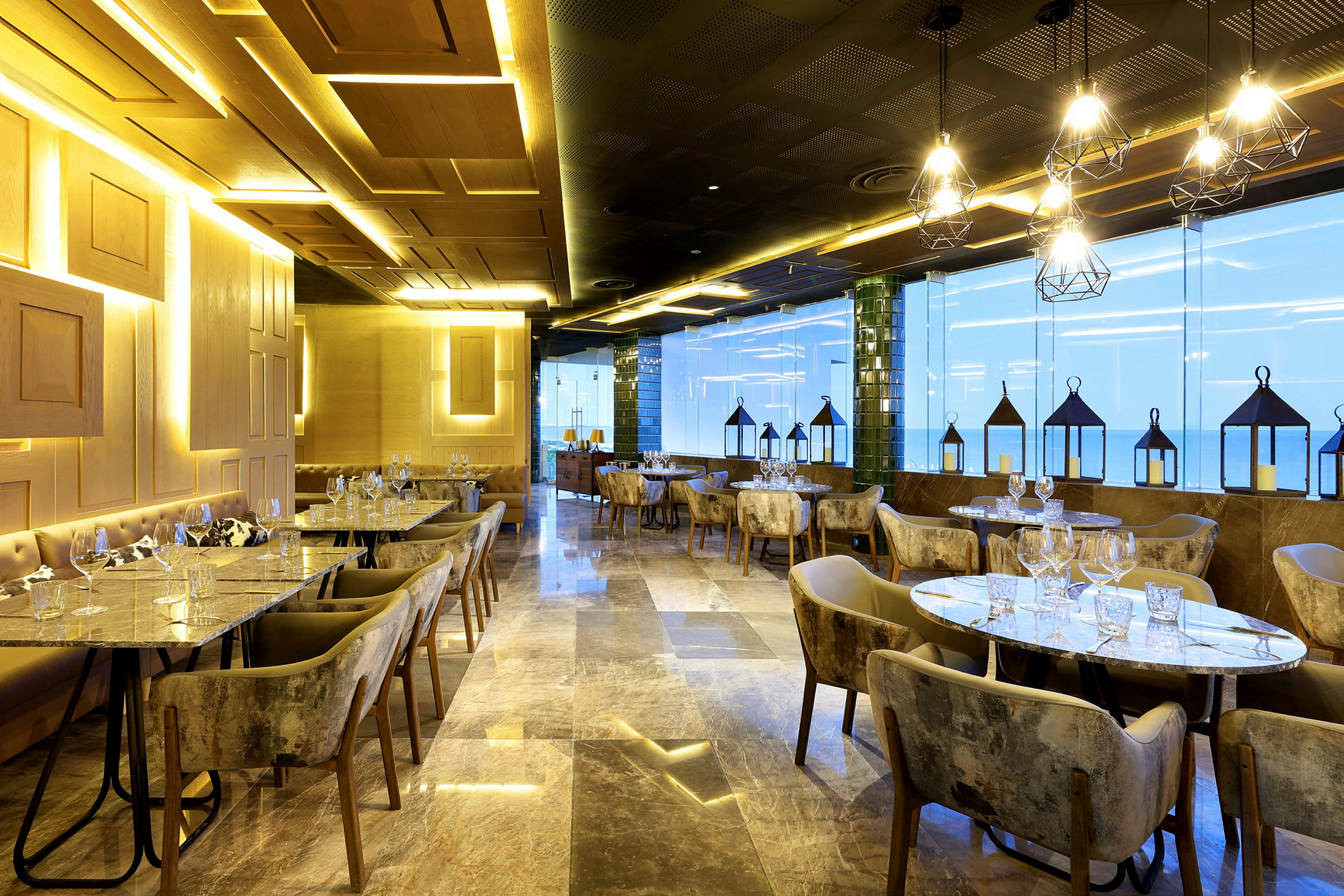 Interiøret i en elegant restaurant med belysning, moderne bord og stoler. Store vinduer med lykter foran. (AI-generert tekst)