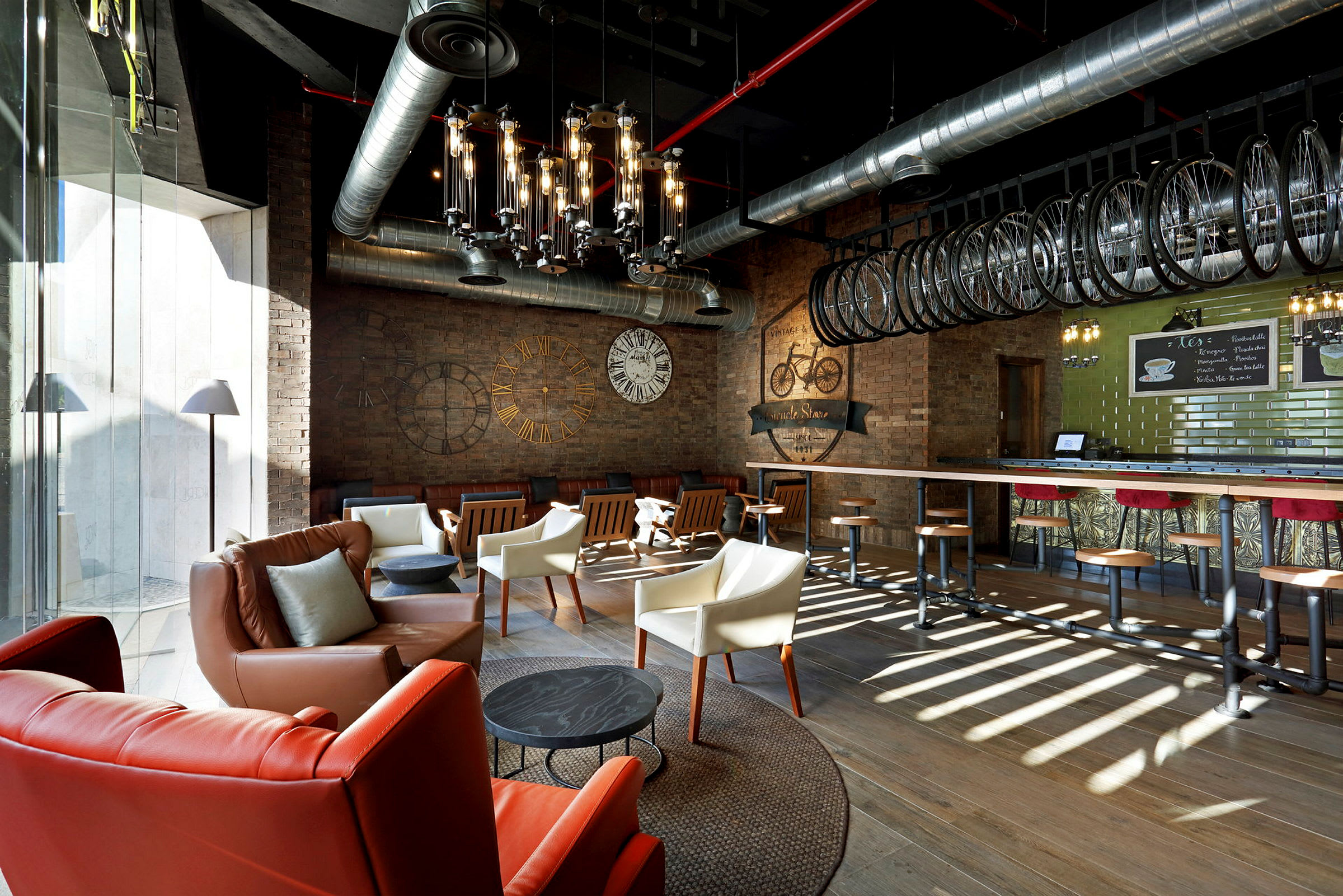 Et interiør av en moderne kaffebar med møblerte sitteplasser, synlige ventilasjonsrør og et industrielt design tema. (AI-generert tekst)