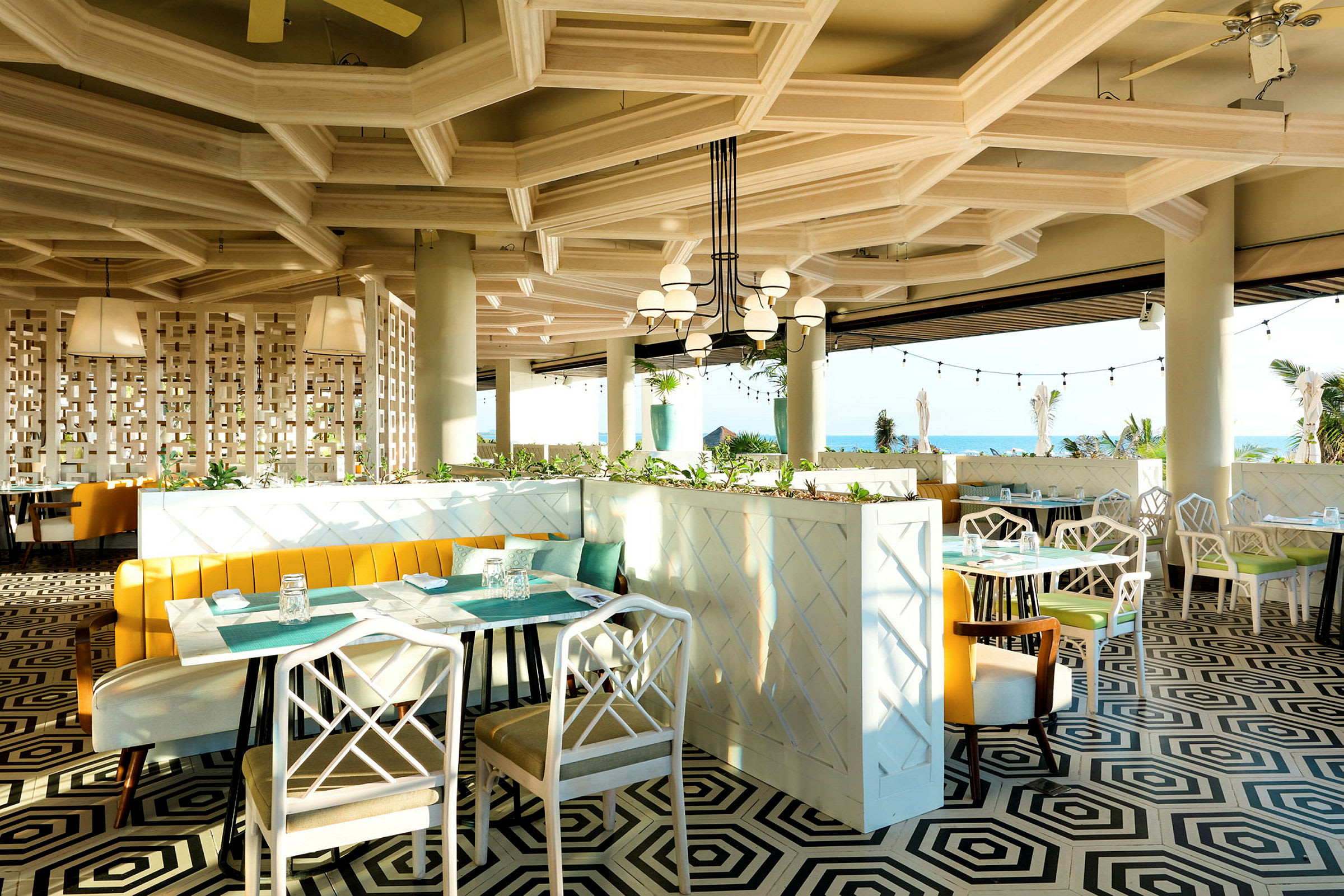 En moderne restaurant med geometrisk mønstret gulv, lyse møbler og store panoramavinduer med utsikt mot havet. (AI-generert tekst)