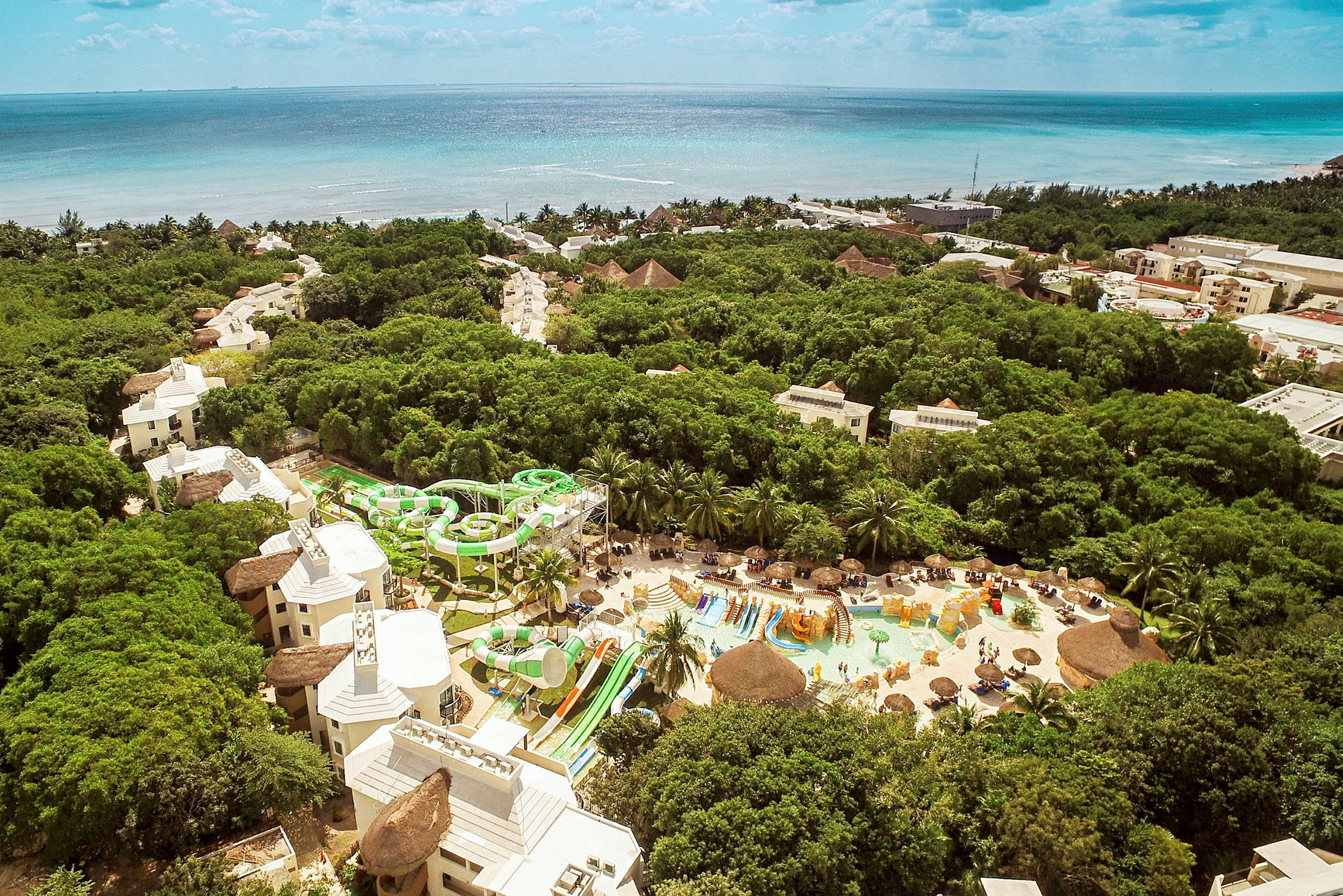 Luftfoto av en resort med basseng- og vannsklieområde omgitt av vegetasjon, med havet i bakgrunnen. (AI-generert tekst)