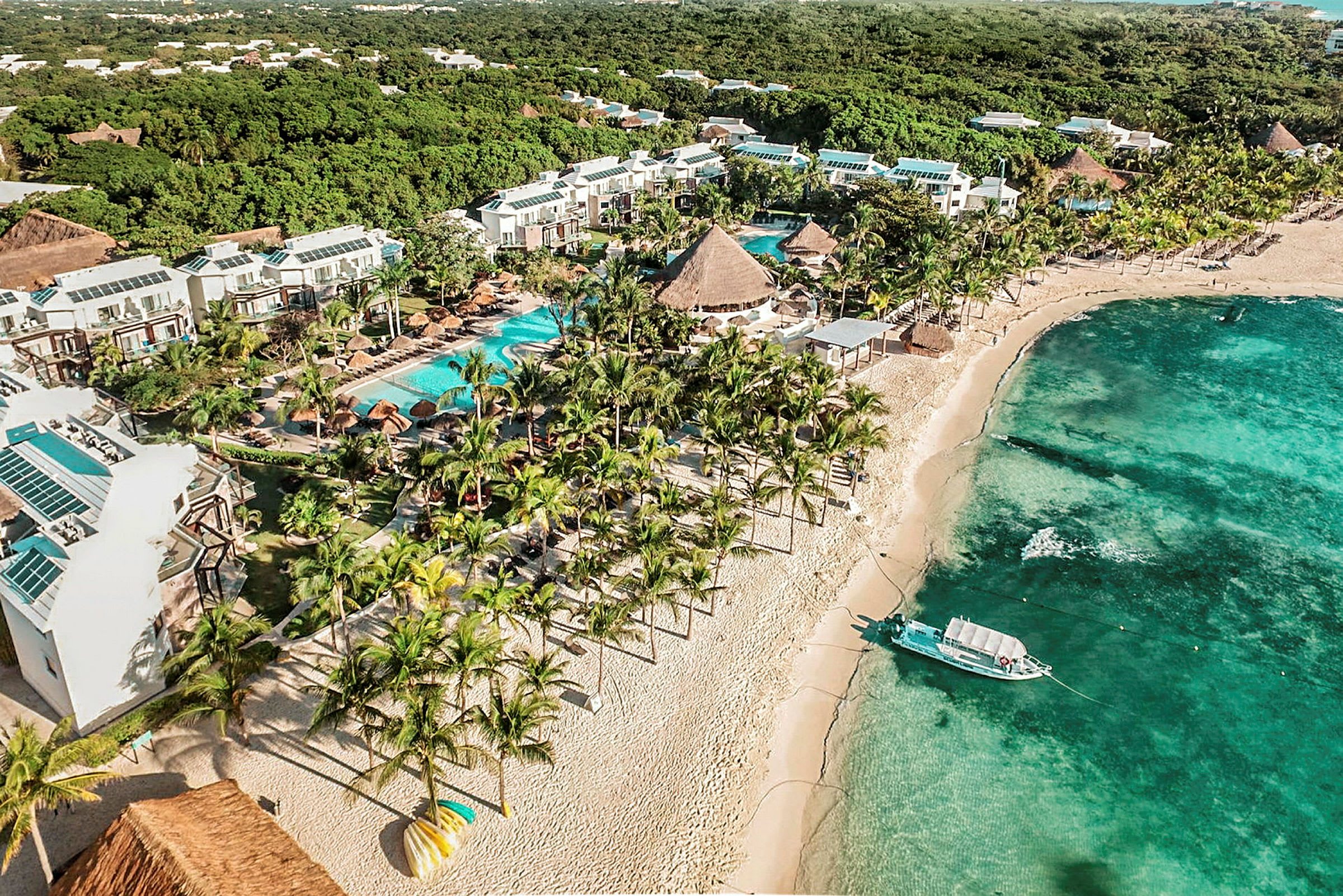 Hotellområde med bassenger og hage ved en sandstrand med turkis vann. (AI-generert tekst)