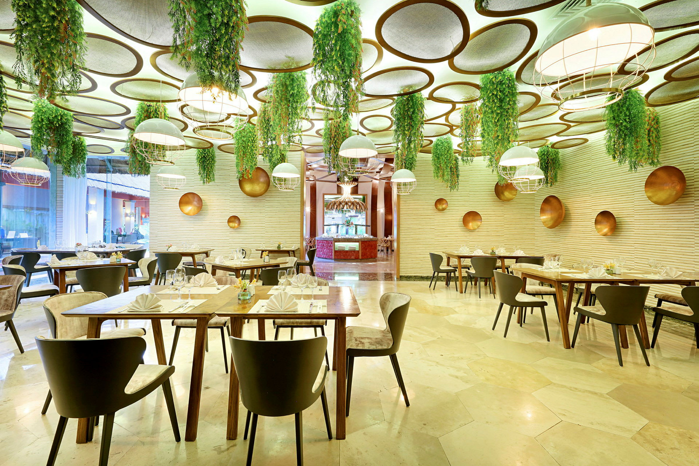 En restaurant med moderne interiør, hvor taket er dekorert med hengende grønne planter og runde paneler. Spisemøblene er stilige, og bordene er dekket. (AI-generert tekst)