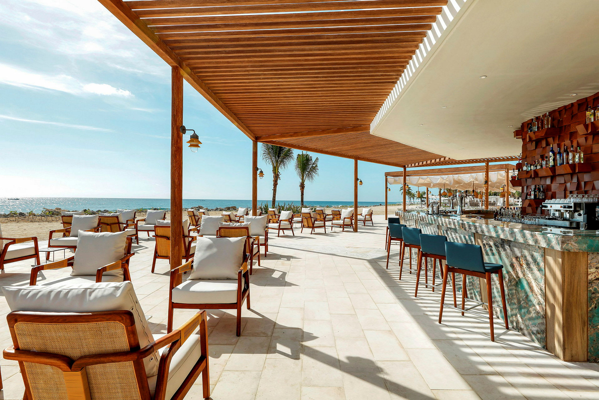 En utendørsrestaurant med sitteplasser og en bar under en trepaviljong ved stranden. (AI-generert tekst)