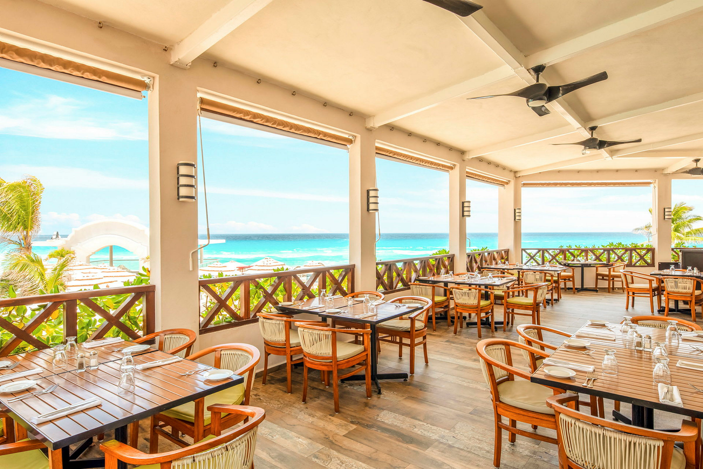 Restaurant med terrasse med bord og stoler, utsikt over havet og stranden. (AI-generert tekst)