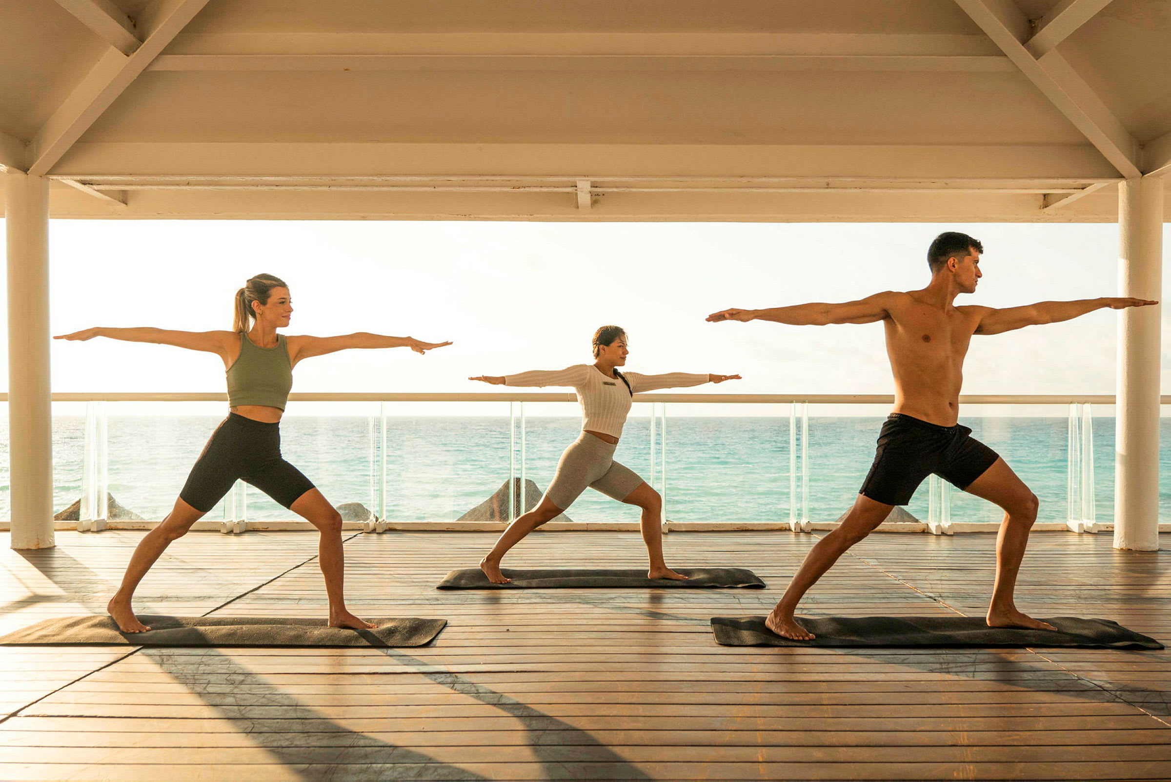 Personer trener yoga på en terrasse med havet i bakgrunnen. (AI-generert tekst)
