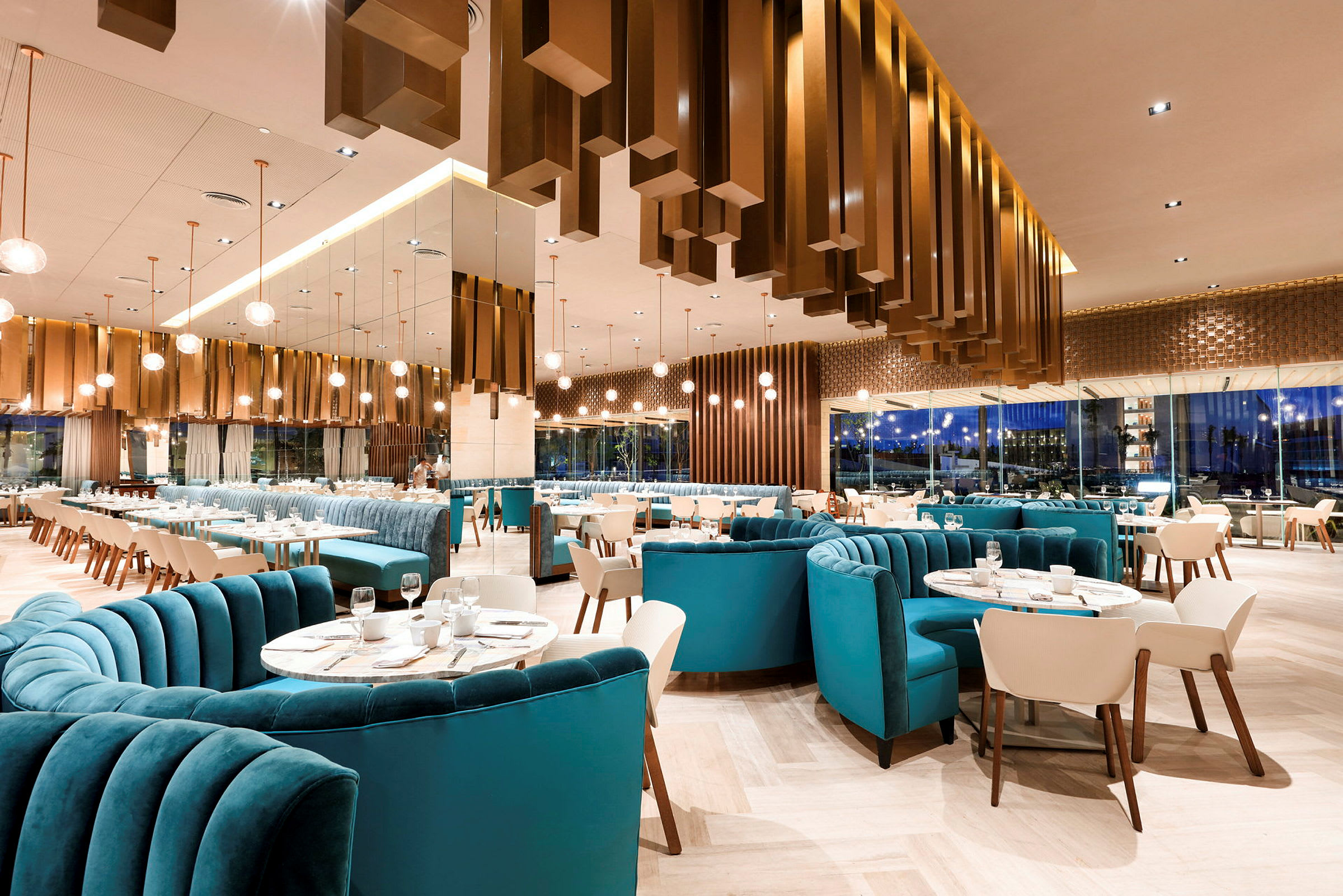 En moderne restaurant med elegante møbler, blå polstrede sofaer og hvite stoler, samt tallerkener og vinglass plassert på bordene. (AI-generert tekst)