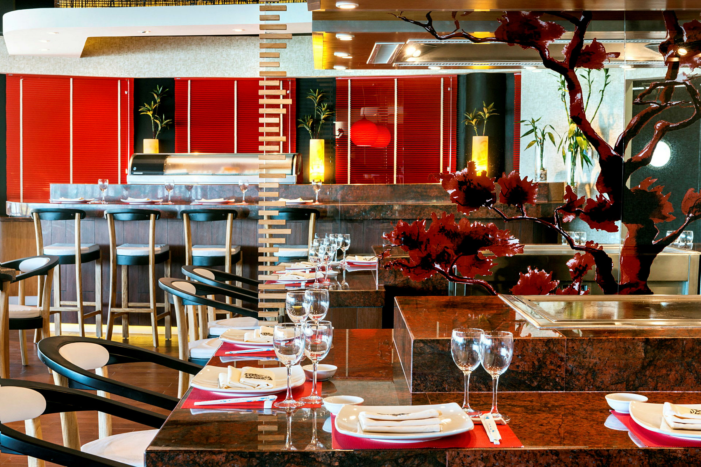 En stilfull restaurantinteriør med bord sett med glass og tallerkener, samt stoler. En bar med stoler vises i bakgrunnen, og lokalet har dekorative detaljer og lyselementer. (AI-generert tekst)