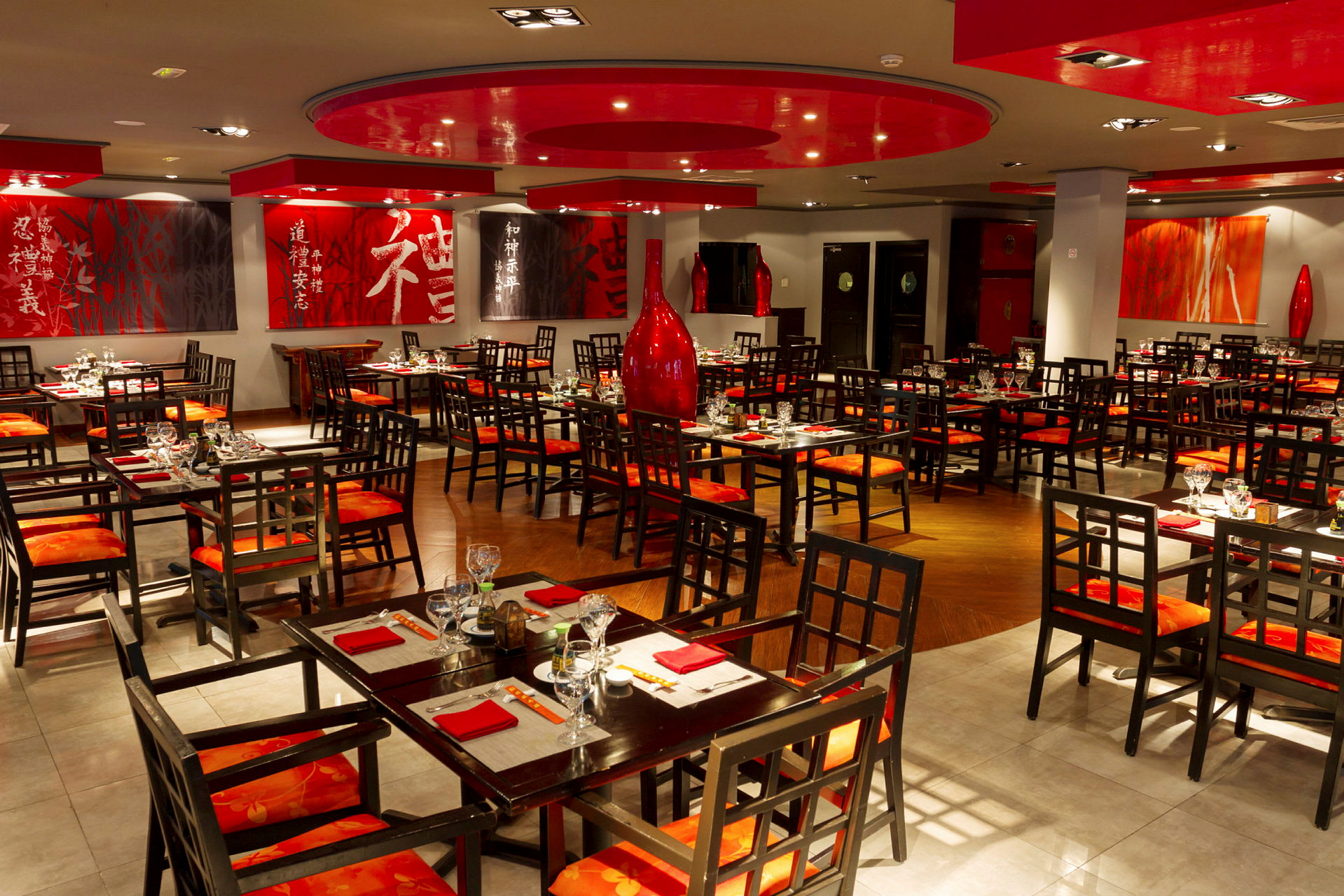 En restaurant med asiatisk innredning og bord- og stolsetter i tre. Veggene er dekorert med kunst og røde detaljer. (AI-generert tekst)
