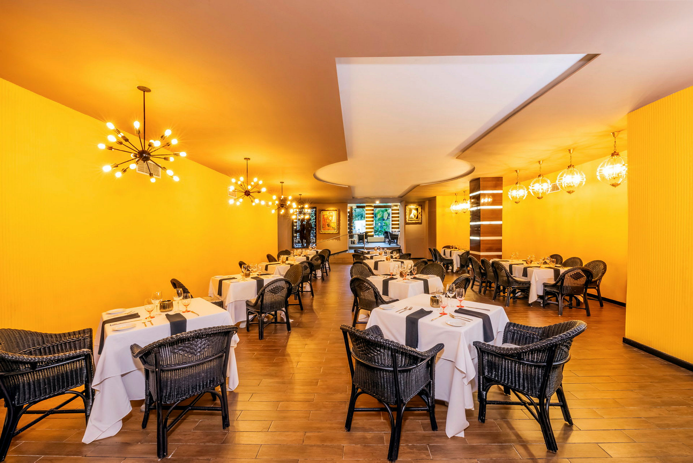 Restaurant med dekte bord og rottingstoler, gul vegg og dekorative lamper. (AI-generert tekst)