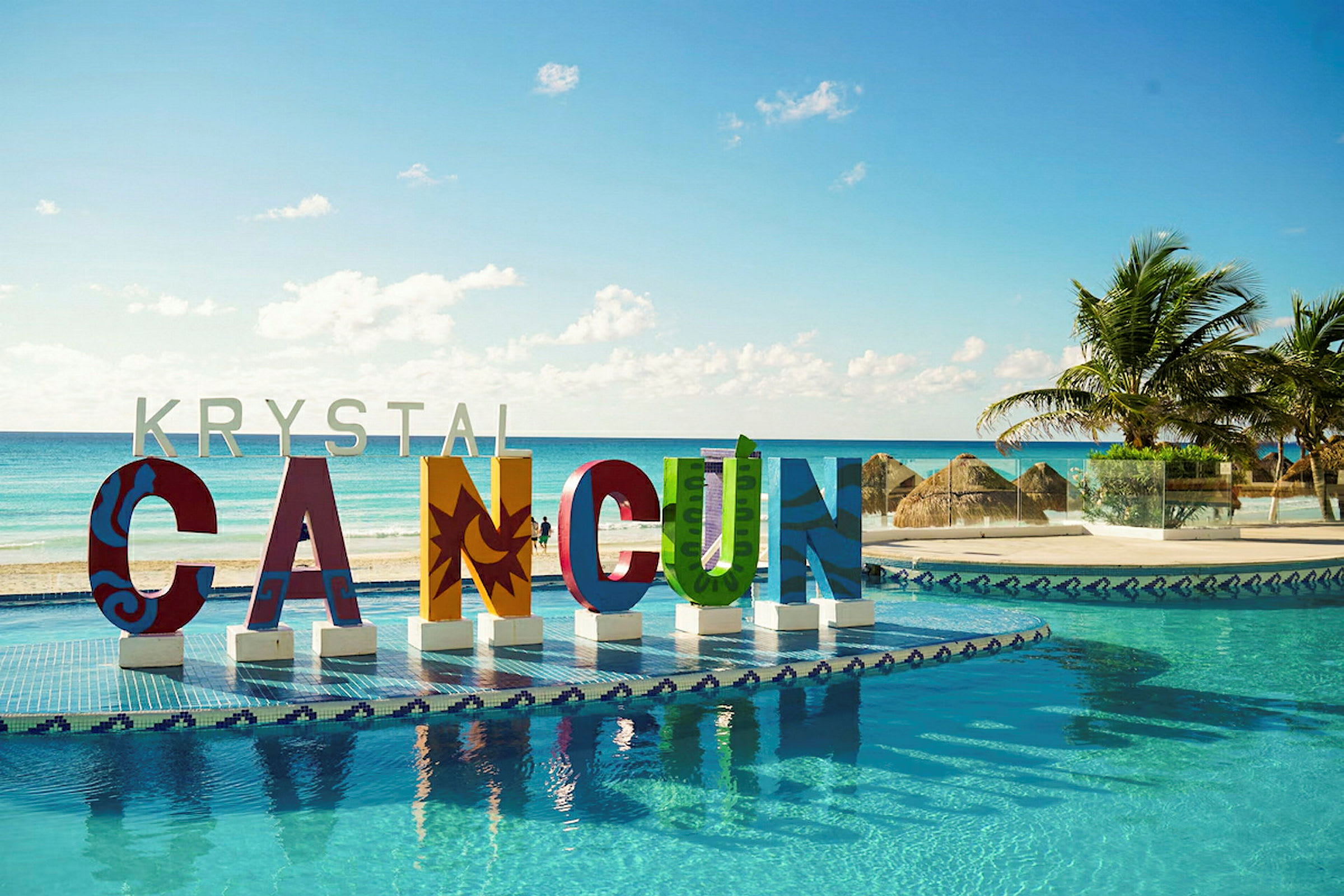 Fargerike bokstaver som danner ordet 'CANCUN' ved et basseng med havutsikt og palmer. (AI-generert tekst)