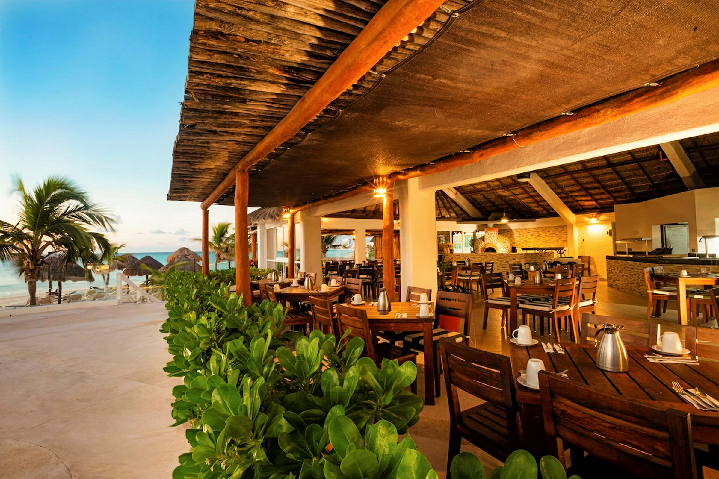 En restaurant med utendørs atmosfære og tremøbler ved stranden, omgitt av grøntområder. (AI-generert tekst)