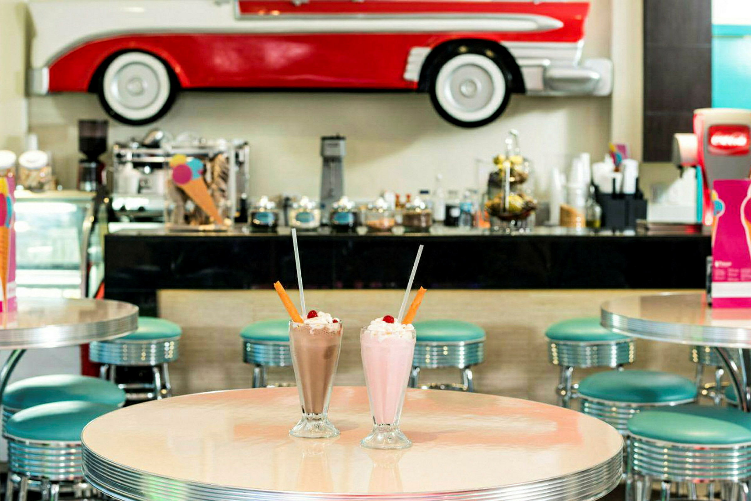 Bilde av en retro interiørkafé med bord og stoler samt milkshakes i forgrunnen. (AI-generert tekst)