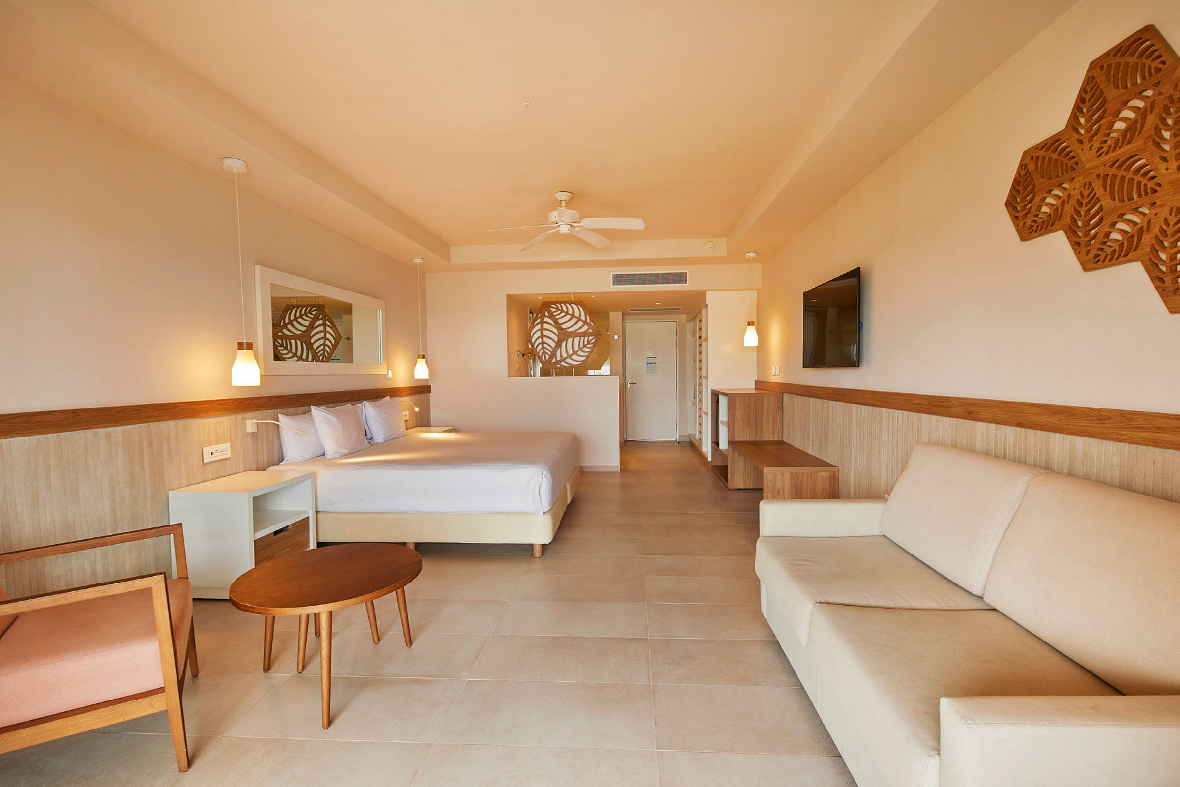 Hotellrom med lys innredning, en seng, sofa og bord samt dekorative veggdetaljer. (AI-generert tekst)