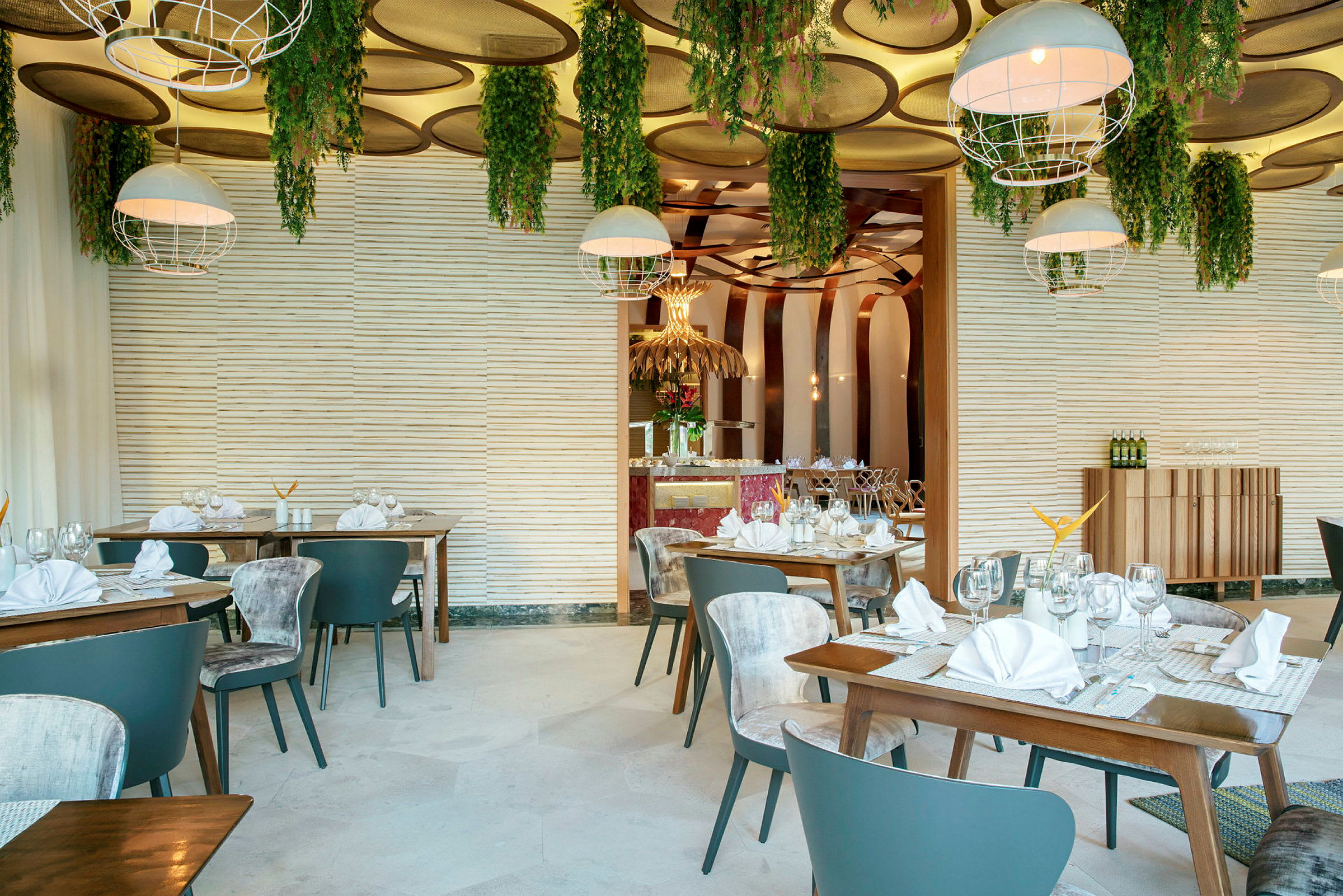 Et moderne og stilfullt designet restaurantområde med trebord og stoler. Dekorasjonene inkluderer hengende plantearrangement fra taket og hvite lampeskjermer. (AI-generert tekst)