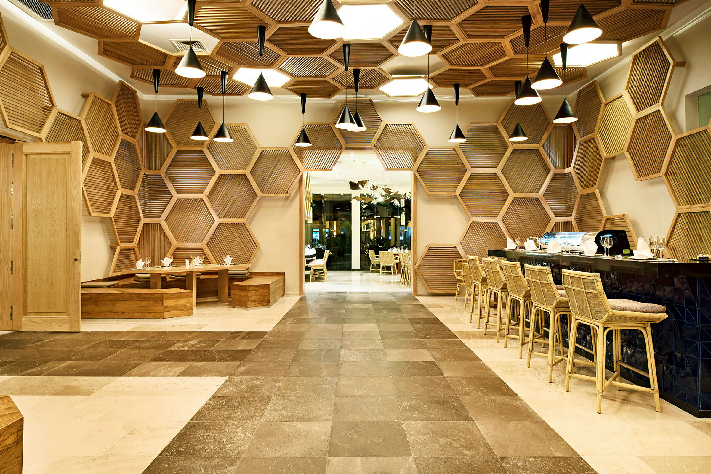 En restaurant med moderne design, sekskantede trepaneler på veggene og taket og elegante taklamper. Bord og stoler i tre er plassert på begge sider. (AI-generert tekst)