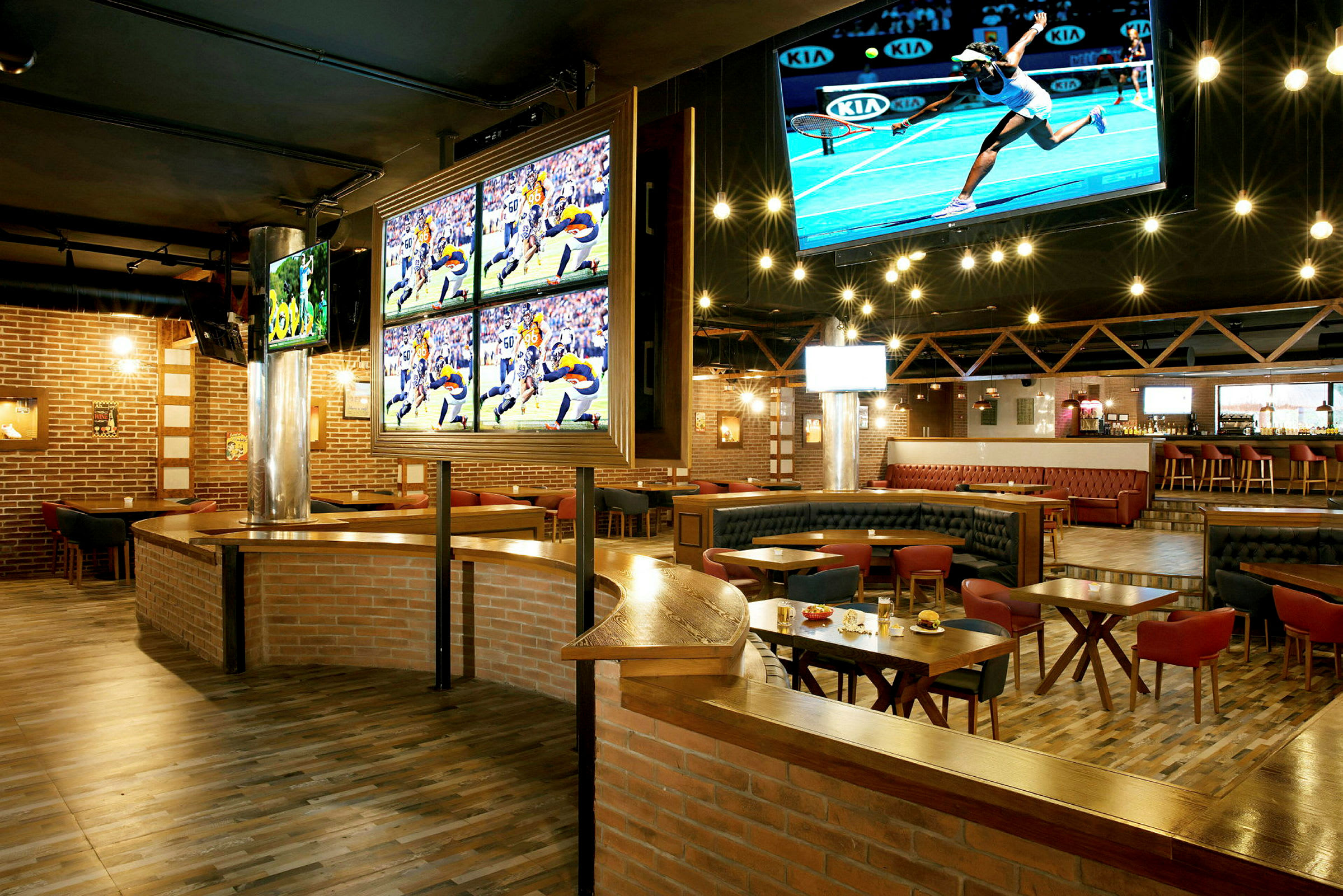 En sportsbar med TV-skjermer som viser ulike sportsarrangementer. Rommet har trebord, komfortable sitteplasser og en bar i bakgrunnen. (AI-generert tekst)
