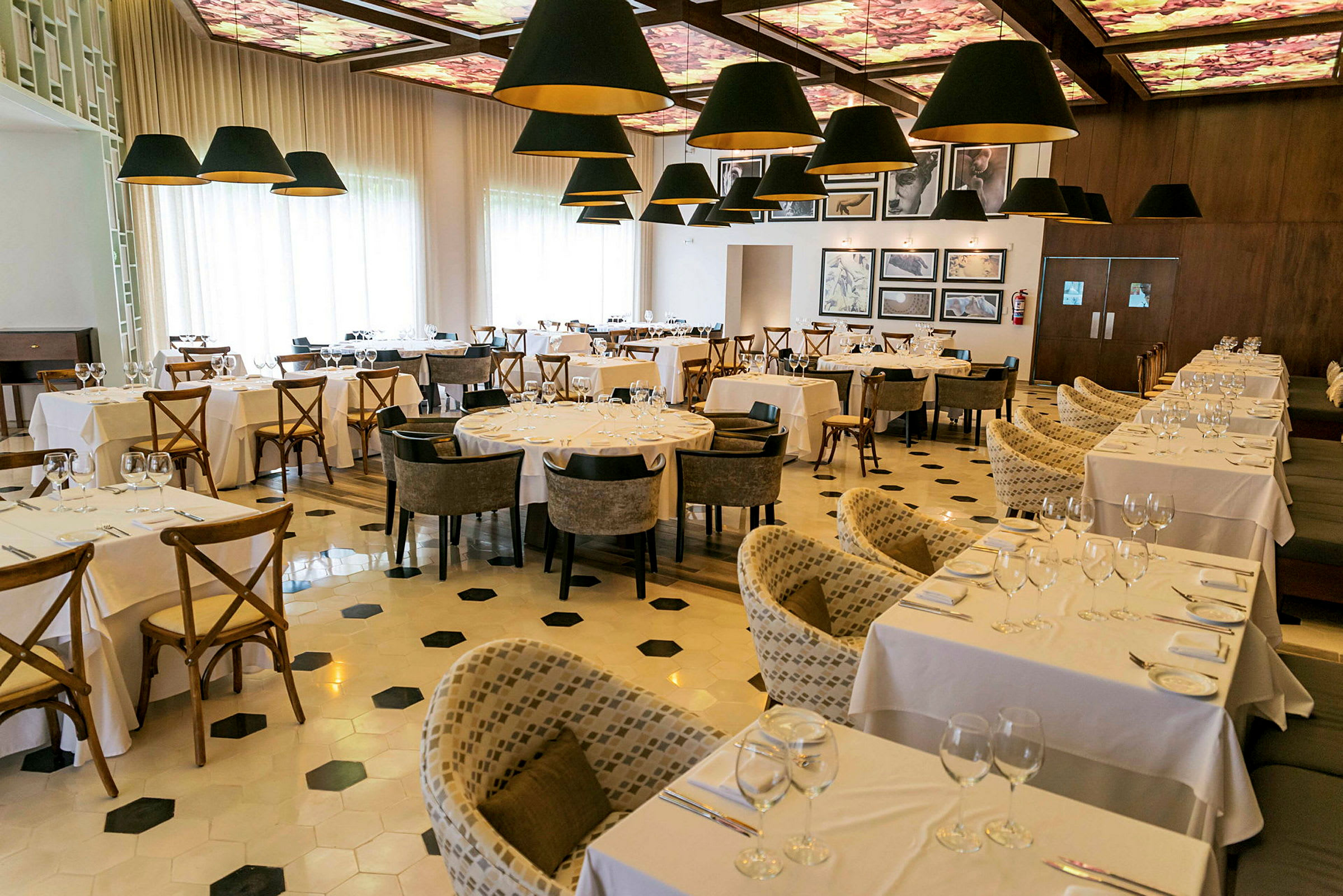 Bilde av en elegant restaurant innredet med hvite duker på bordene og komfortable stoler, med dekorative lamper som henger fra taket. (AI-generert tekst)