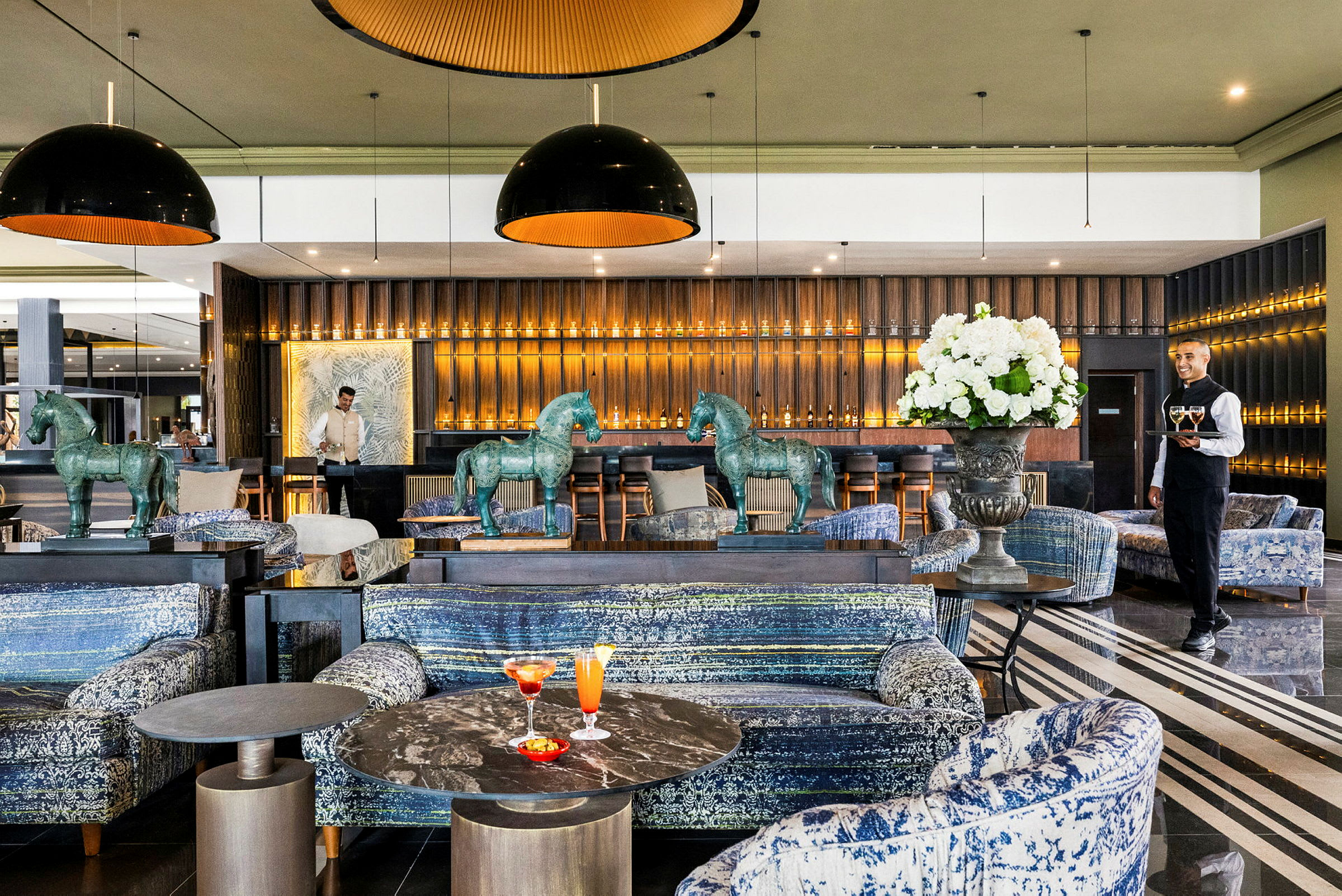 En stilfull lounge med sofaer, marmorbord og dekorative hestestatuer, samt en bar belyst med varme lys. (AI-generert tekst)