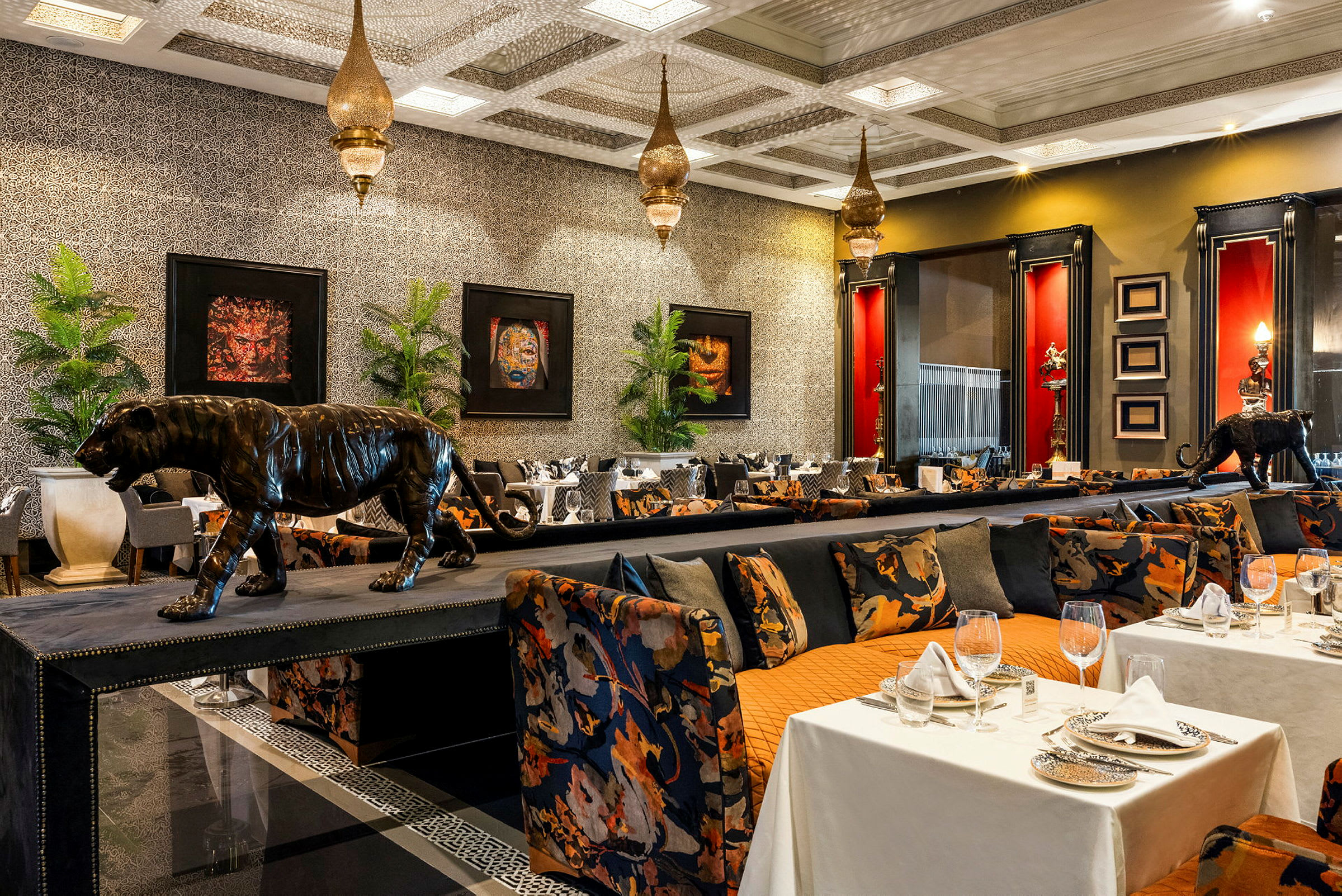 Bilde av en elegant restaurant med et eksotisk tema, inkludert dekorasjoner med leopardstatuer, forgylte lamper og fargerike møbler. (AI-generert tekst)