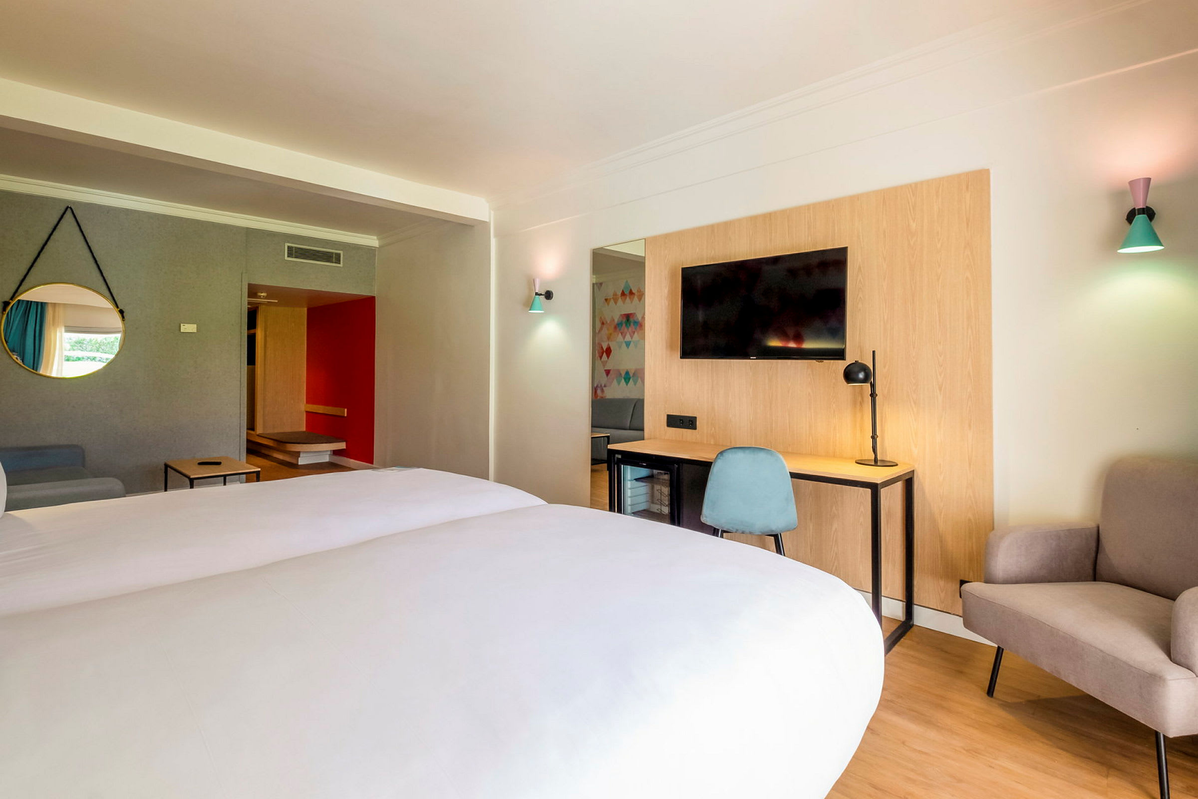 Hotellrom med dobbeltseng, skrivebord og stol, TV samt sitteplass. (AI-generert tekst)