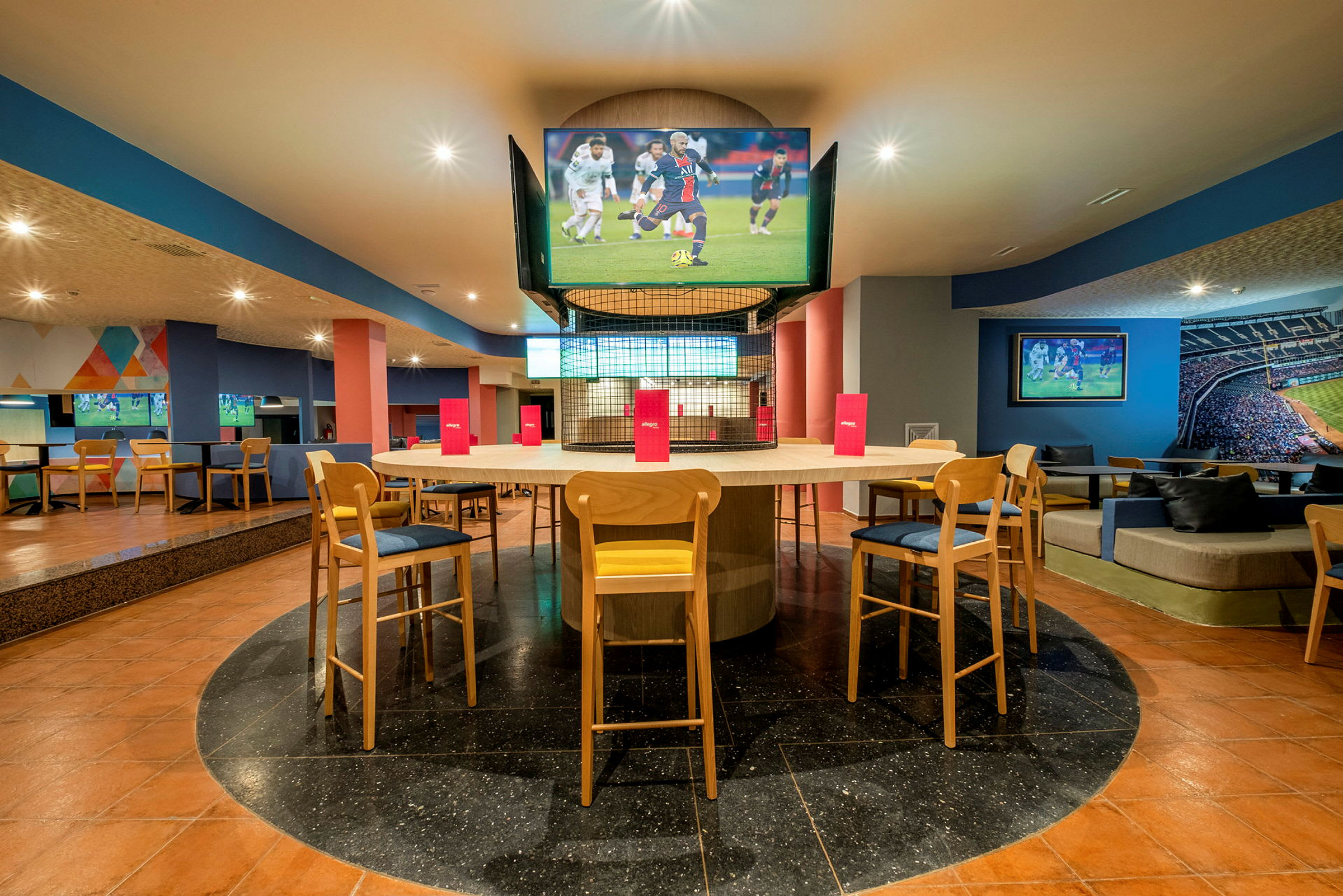 Interiør av en moderne sportsbar med sitteplasser rundt et bord og flere TV-skjermer. (AI-generert tekst)