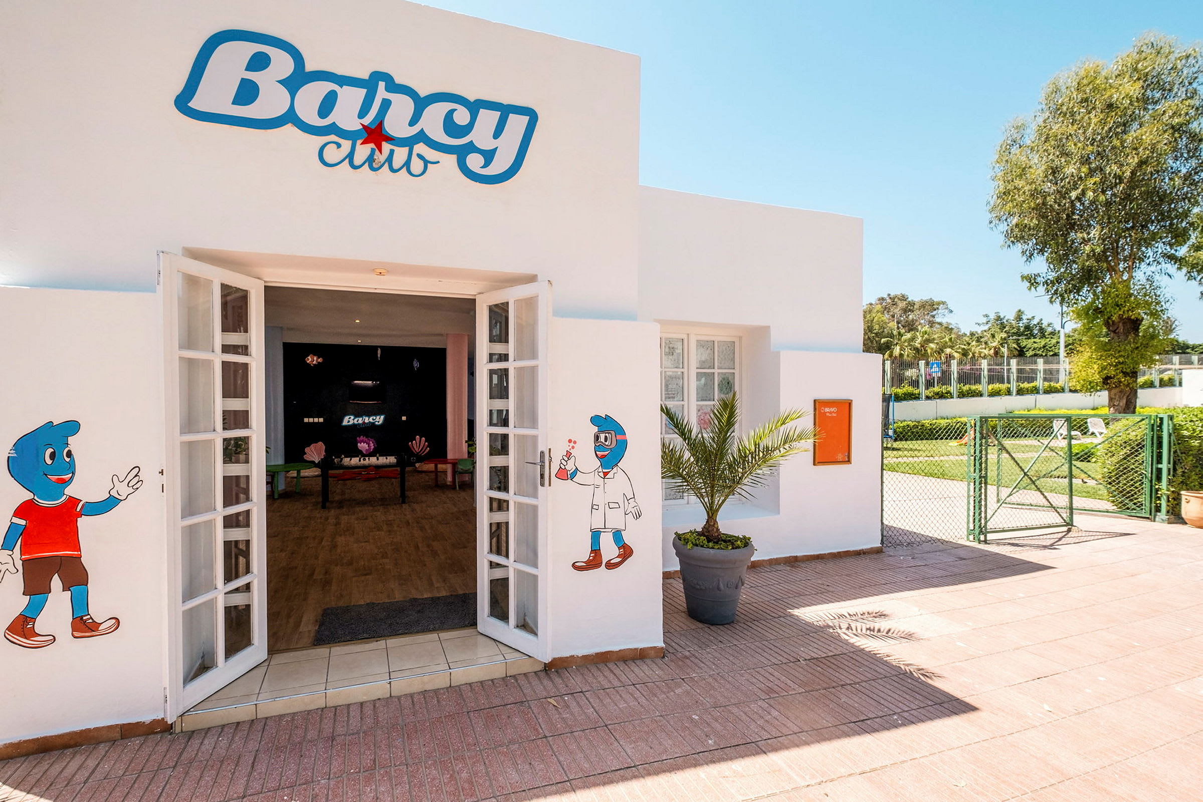 Inngang til Barcy Club med dekorasjoner på veggene og en gårdsplass med grøntområder. (AI-generert tekst)
