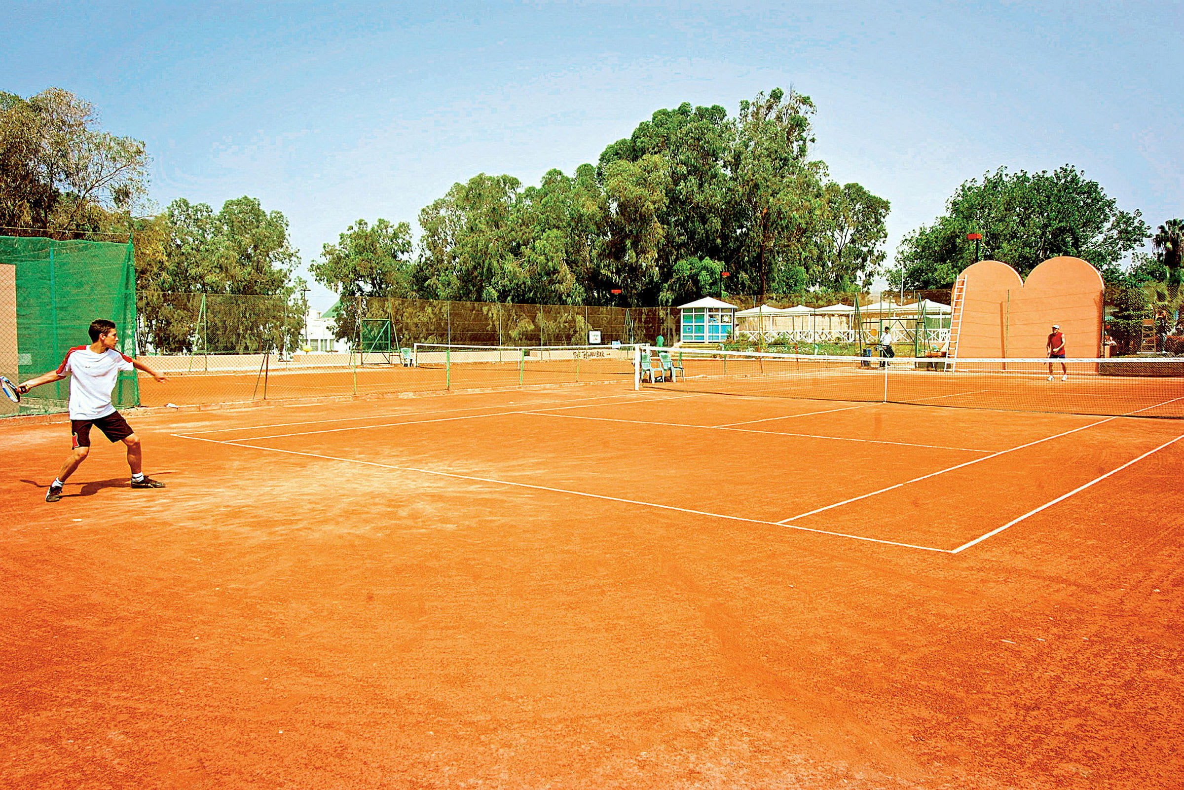 En utendørs tennisbane med to personer som spiller tennis. (AI-generert tekst)