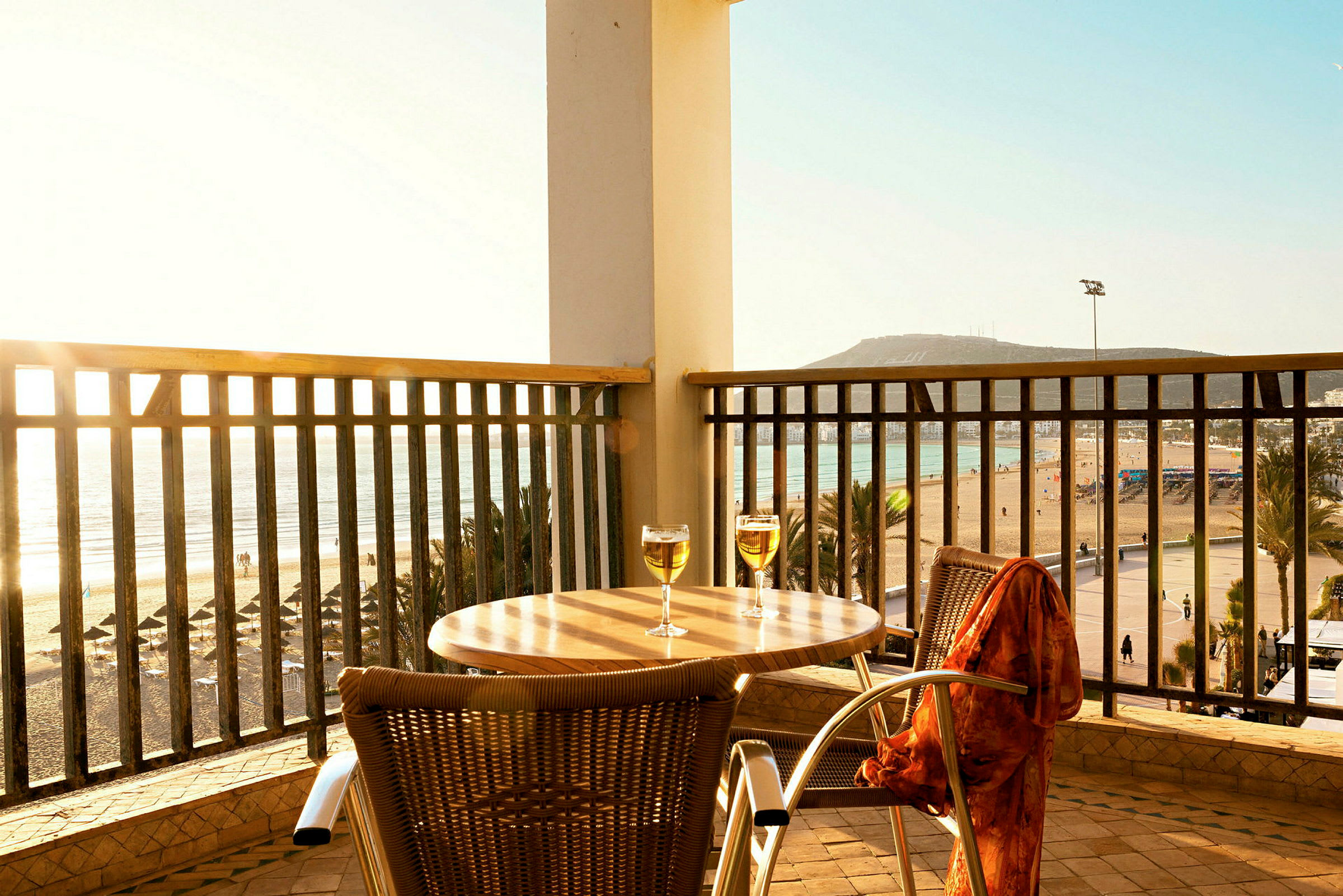 En terrasse med et bord og to glass, med utsikt over en strand og havet. (AI-generert tekst)