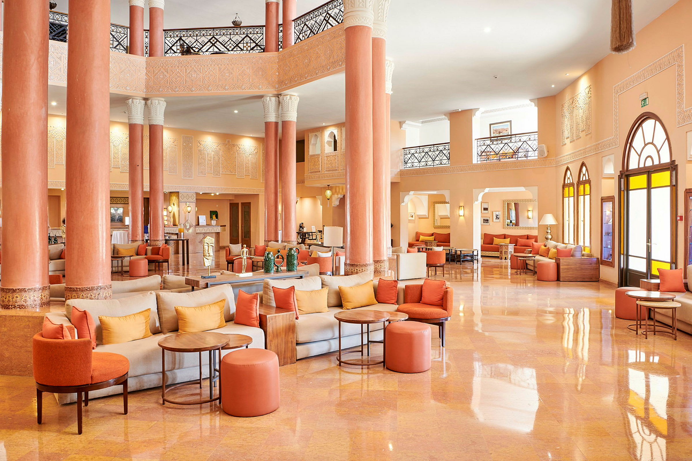 Hotellobby med oransje og beige farger, sittegrupper og søyler. (AI-generert tekst)