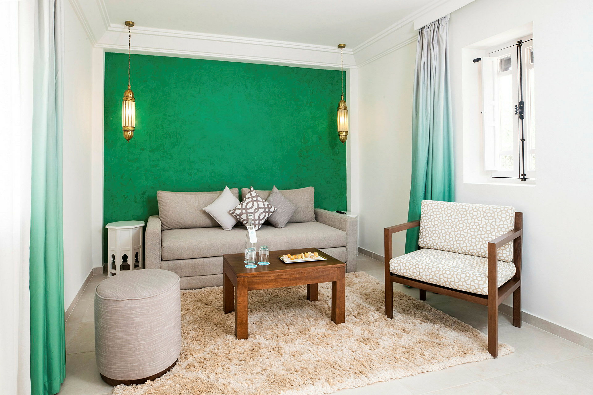 Et stue med grønn vegg, en beige sofa, en stol, et lite bord og et teppe. (AI-generert tekst)
