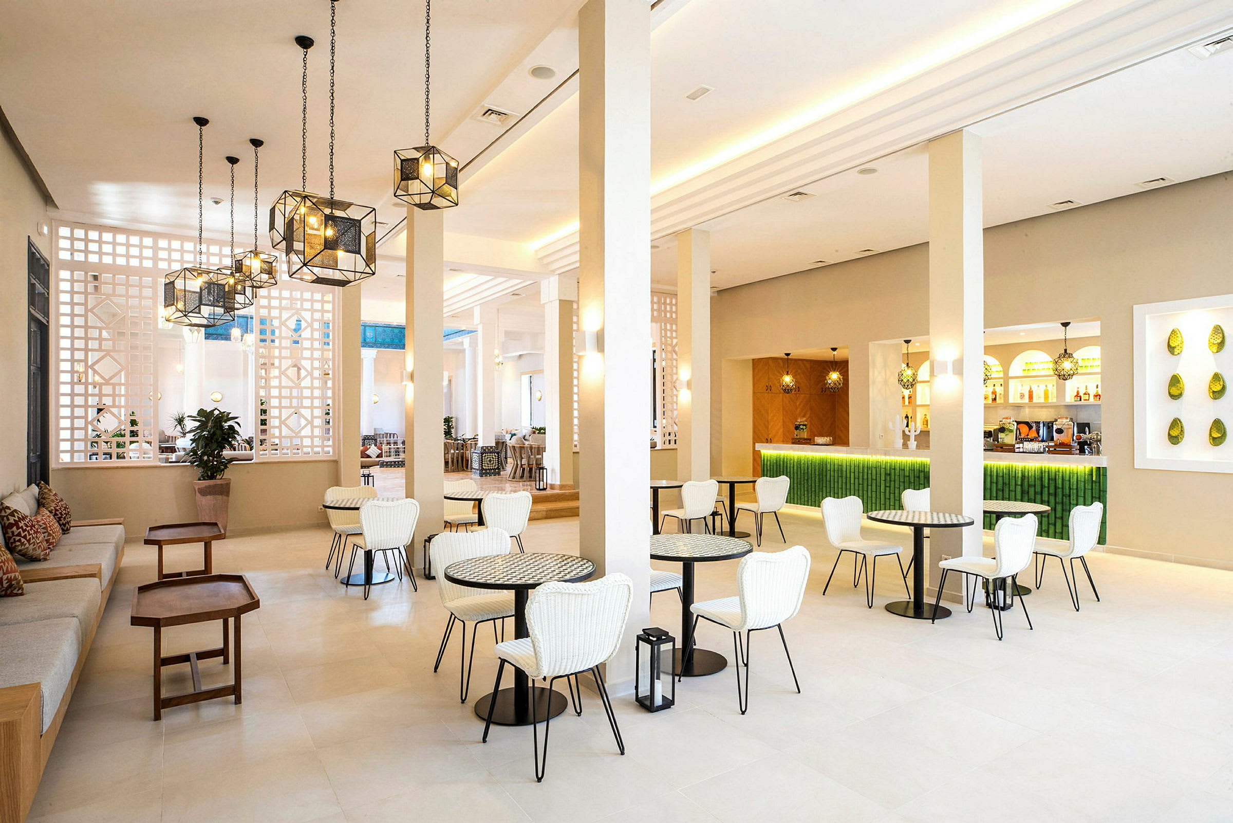 En lys og moderne lounge med hvite stoler, små bord og en grønn bardisk. (AI-generert tekst)