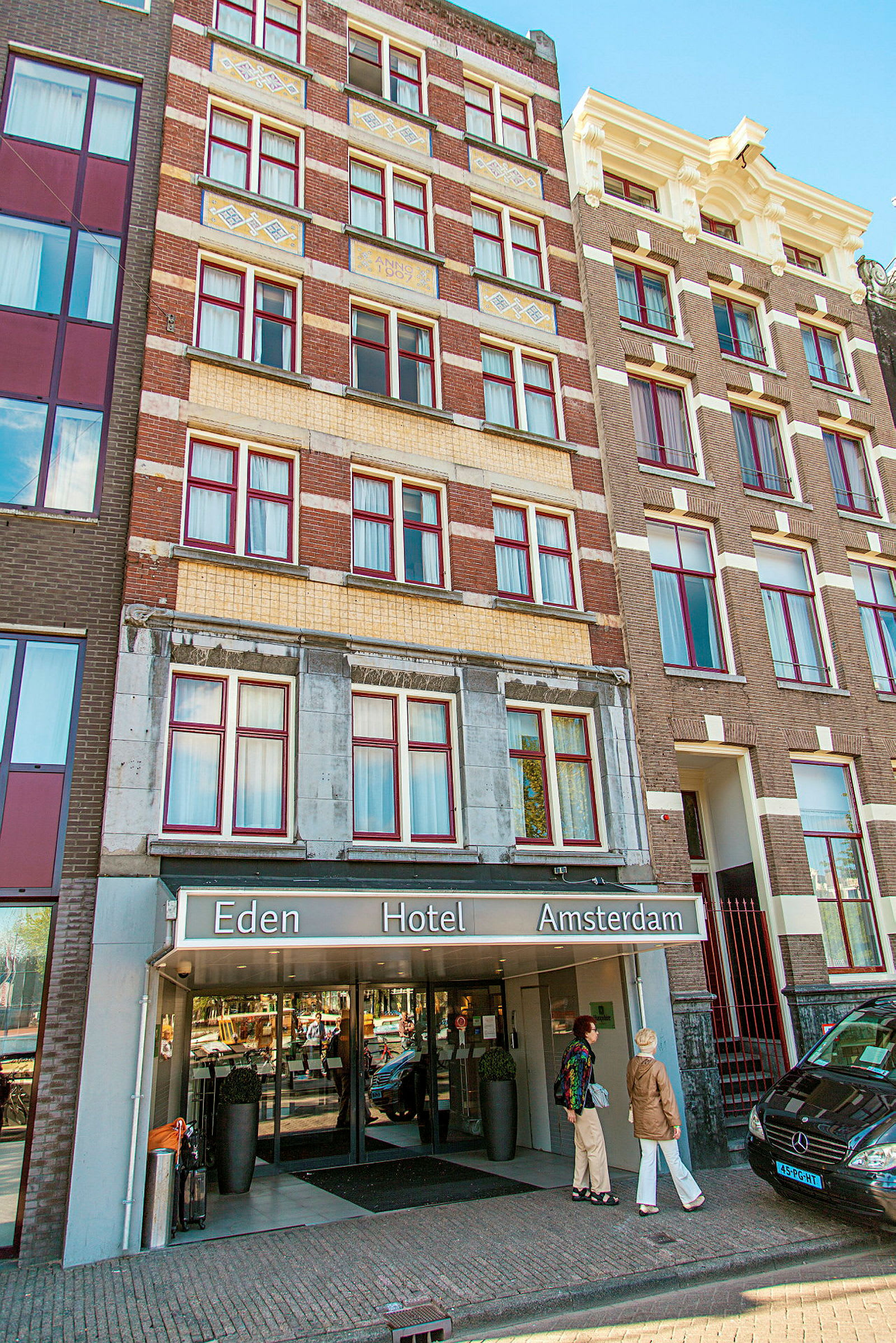 Forsiden av Eden Hotel Amsterdam med inngang og personer foran bygningen. (AI-generert tekst)
