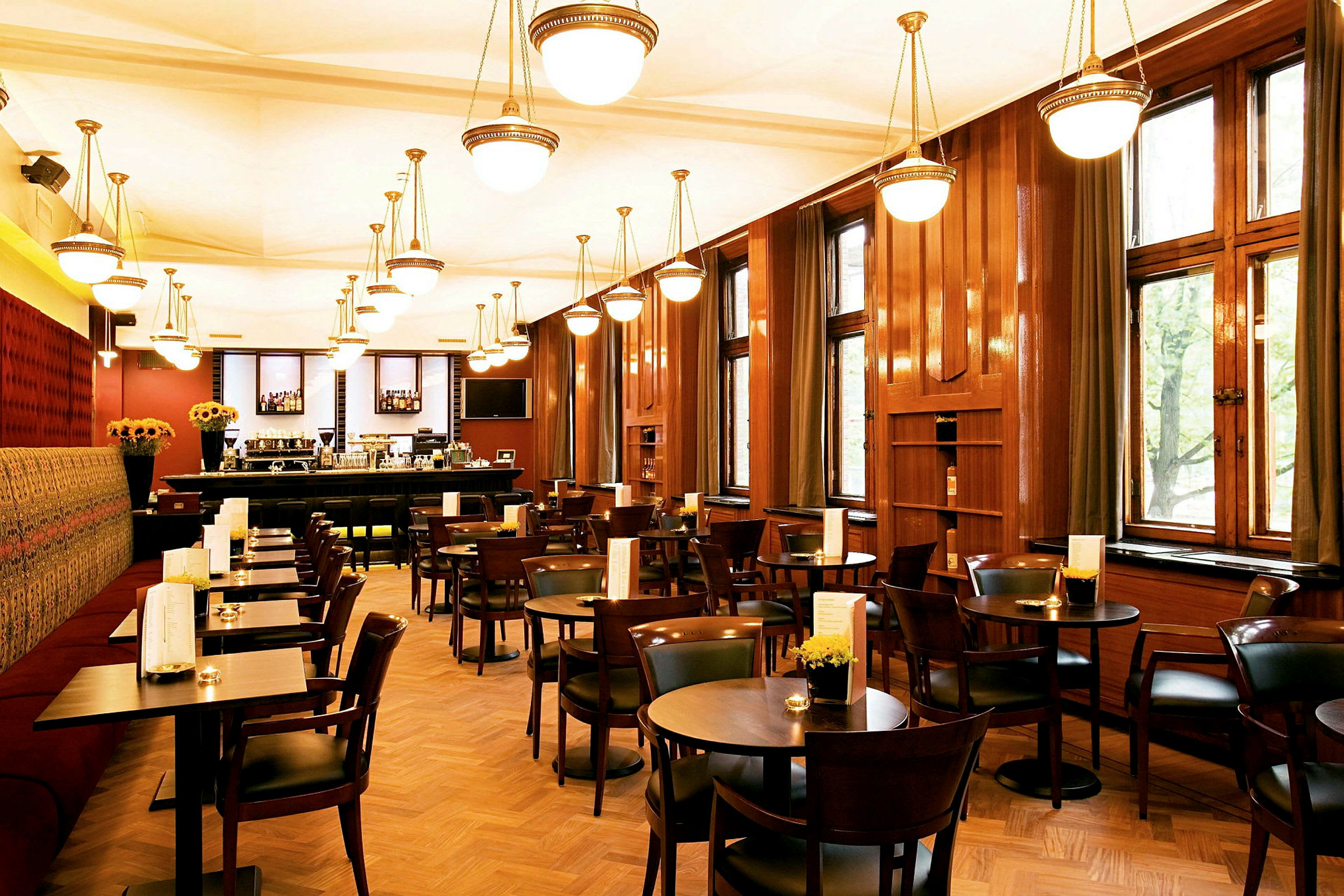 Bilde av en restaurantinteriør med trebord og stoler, store vinduer og hengende lamper i taket. (AI-generert tekst)