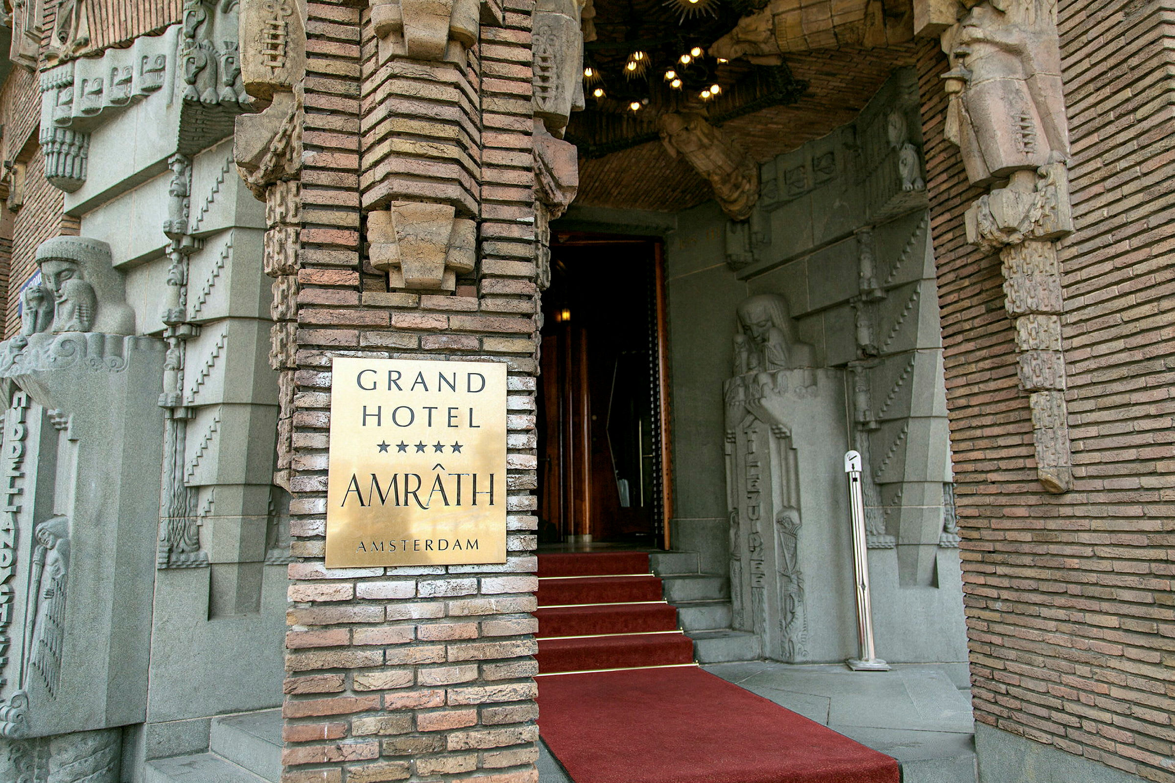 Inngangsdør til Grand Hotel Amrâth Amsterdam med dekorative steinutsmykninger. (AI-generert tekst)