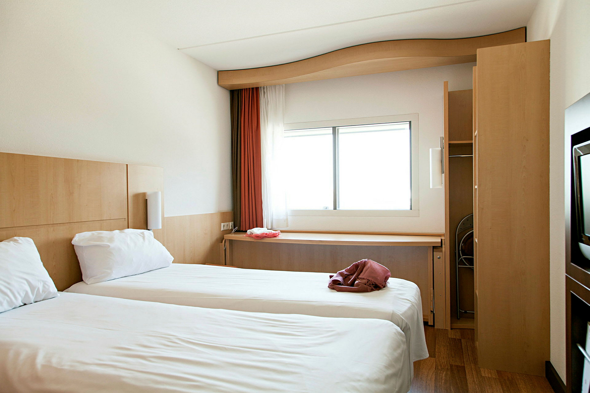 Et hotellrom med to enkeltsenger og et vindu med lysinnslipp. (AI-generert tekst)