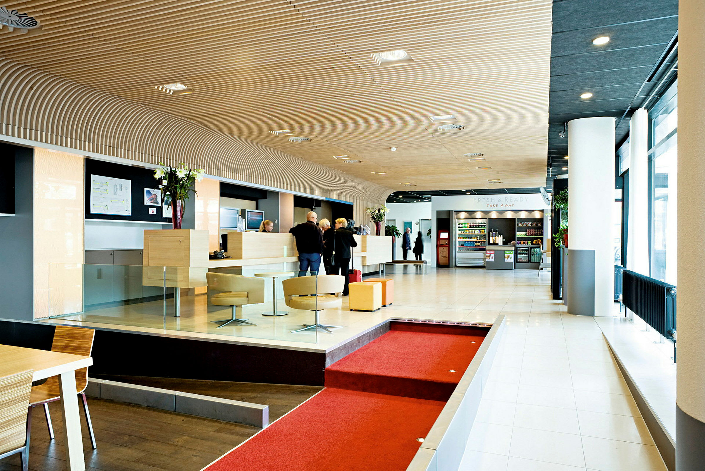 Lys og moderne hotellobby med resepsjon, sittegrupper og en kiosk med drikkevarer og snacks. (AI-generert tekst)