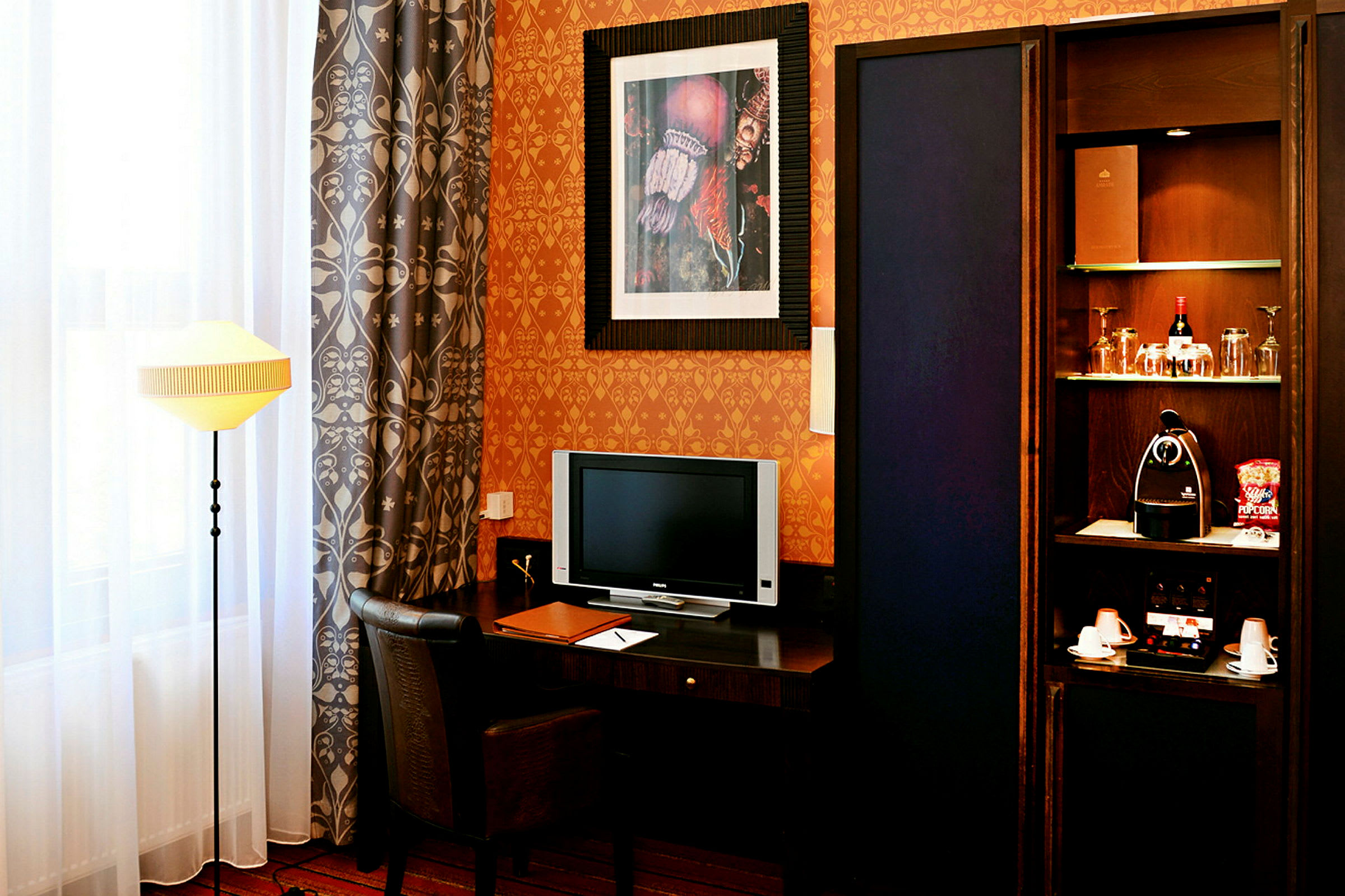 Et hotellrom med skrivebord, stol, TV, bordlampe og et skap med drikke og kaffemaskin. (AI-generert tekst)