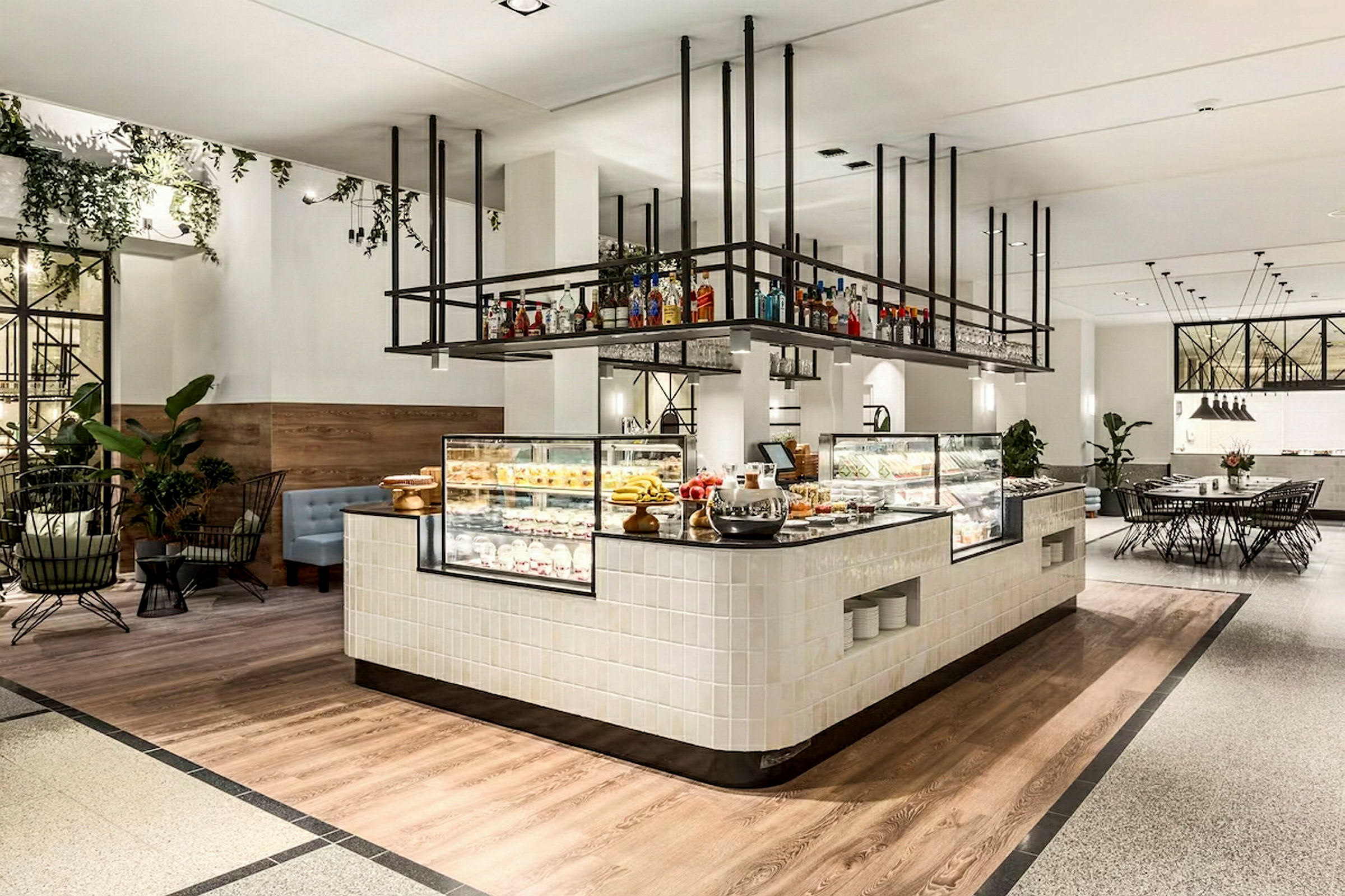 Interiør av en moderne kafé eller restaurant med en serveringsdisk og utstilte bakverk. Møbler inkluderer stoler og bord, samt plantepynt. (AI-generert tekst)