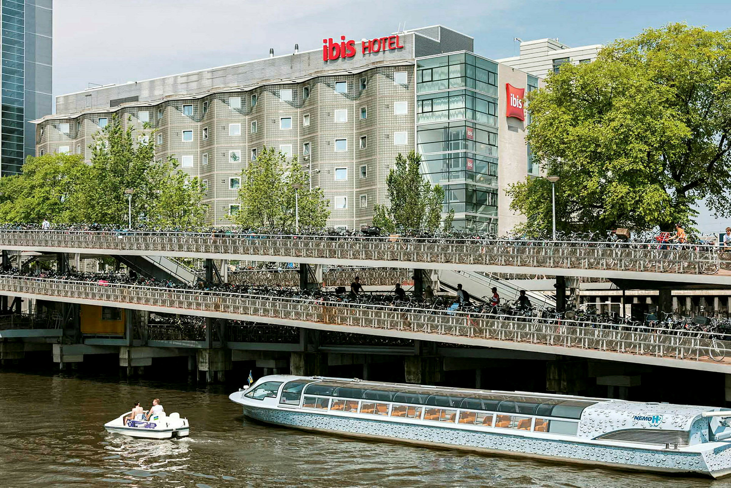 Bilde av en treetasjes sykkelparkering ved siden av en elv, med et hotell i bakgrunnen og båter på vannet. (AI-generert tekst)