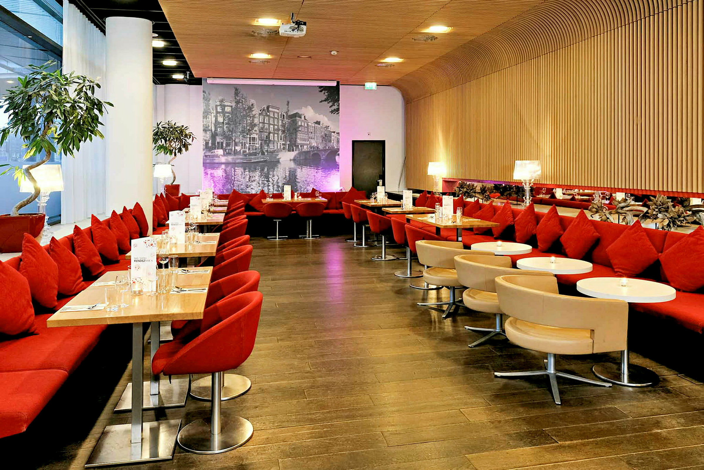 Stemningsfull restaurant med røde sitteplasser, små bord og en bakgrunnsvegg med et svart-hvitt bybilde. (AI-generert tekst)