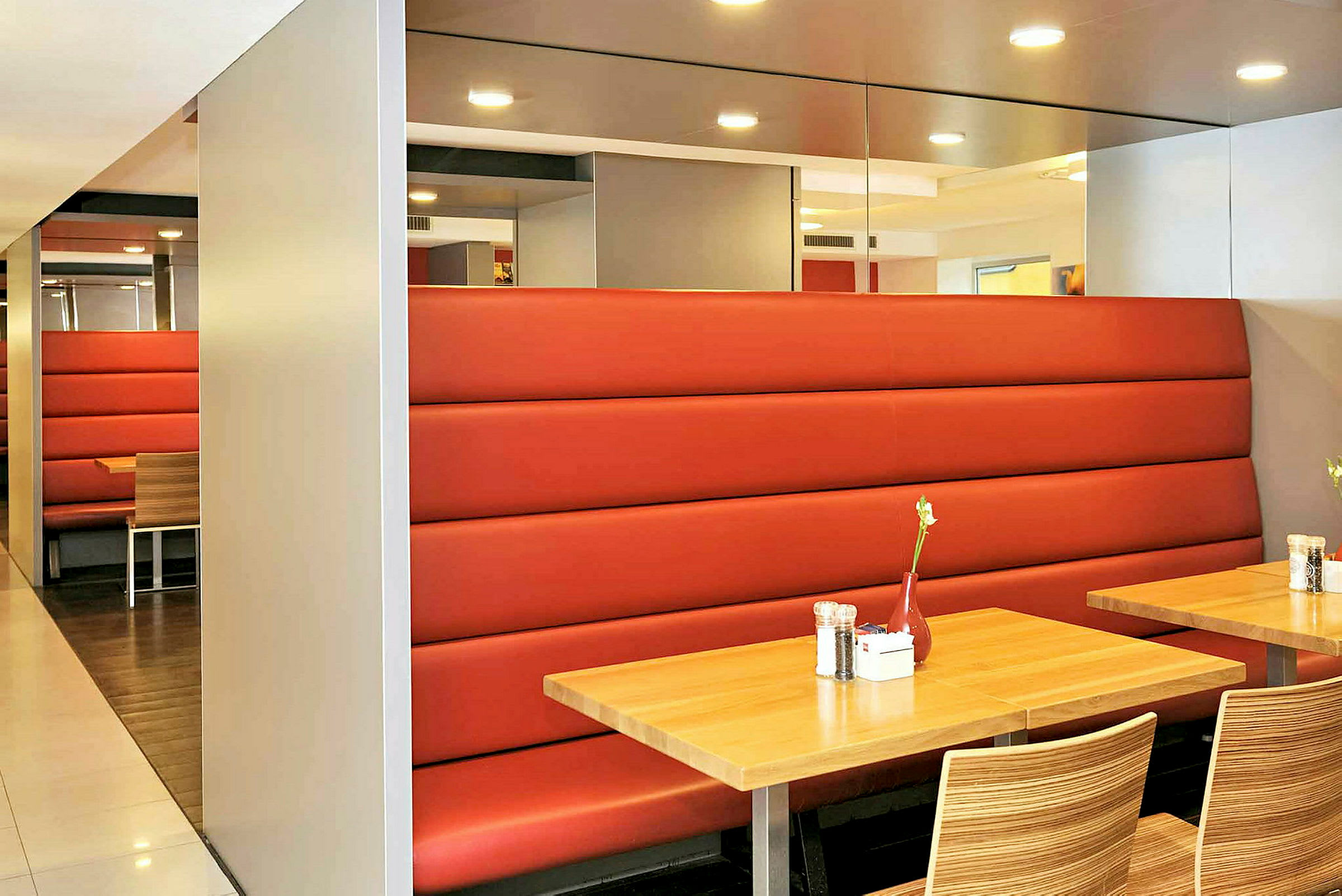 En interiør av en restaurant med trebord, røde sofaer og stoler med tremønster. (AI-generert tekst)