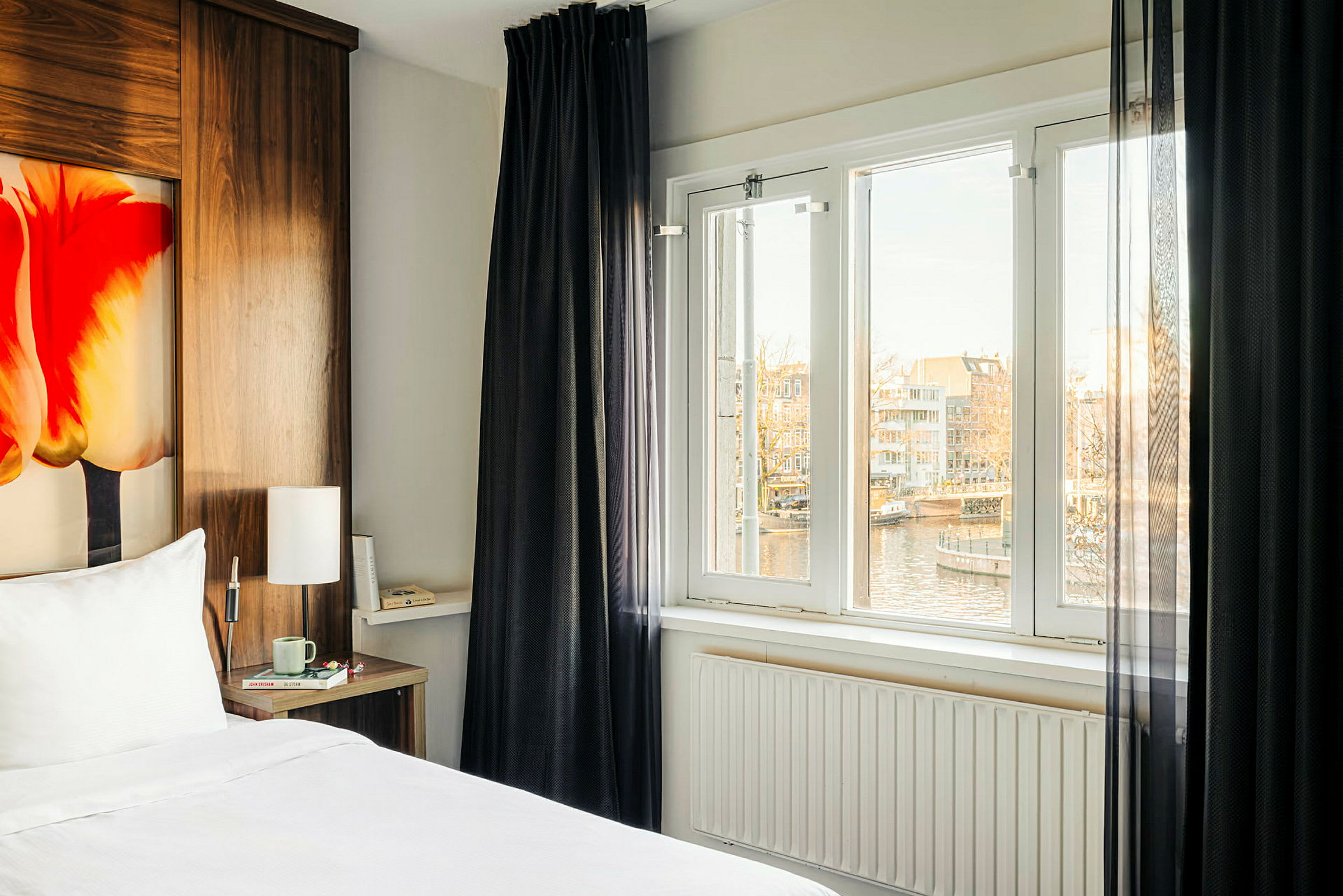Et hotellrom med en seng, et vindu med utsikt over en kanal og hus. (AI-generert tekst)