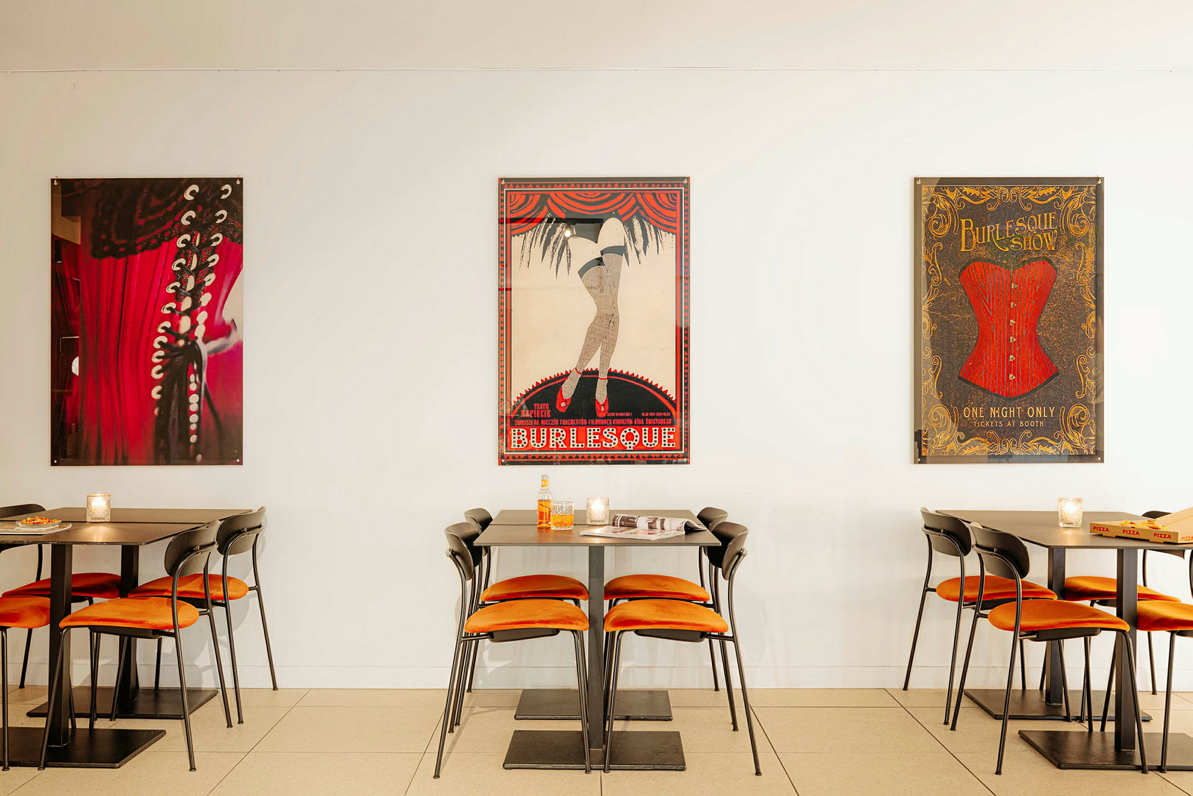 Bilde av et kafémiljø med bord og stoler, samt burlesque-inspirerte plakater på veggen. (AI-generert tekst)